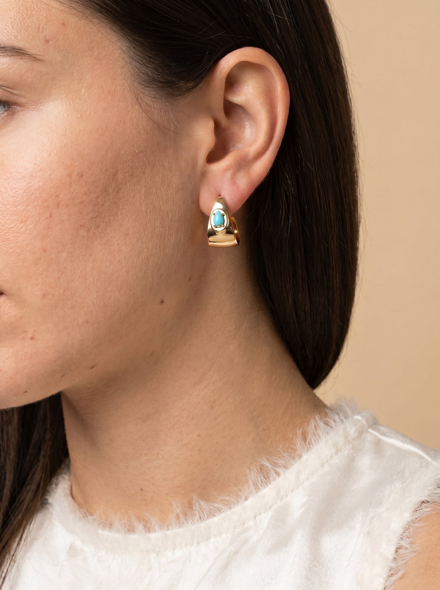 Model wearing gold half hoop earrings with oval turquoise stone, side profile view