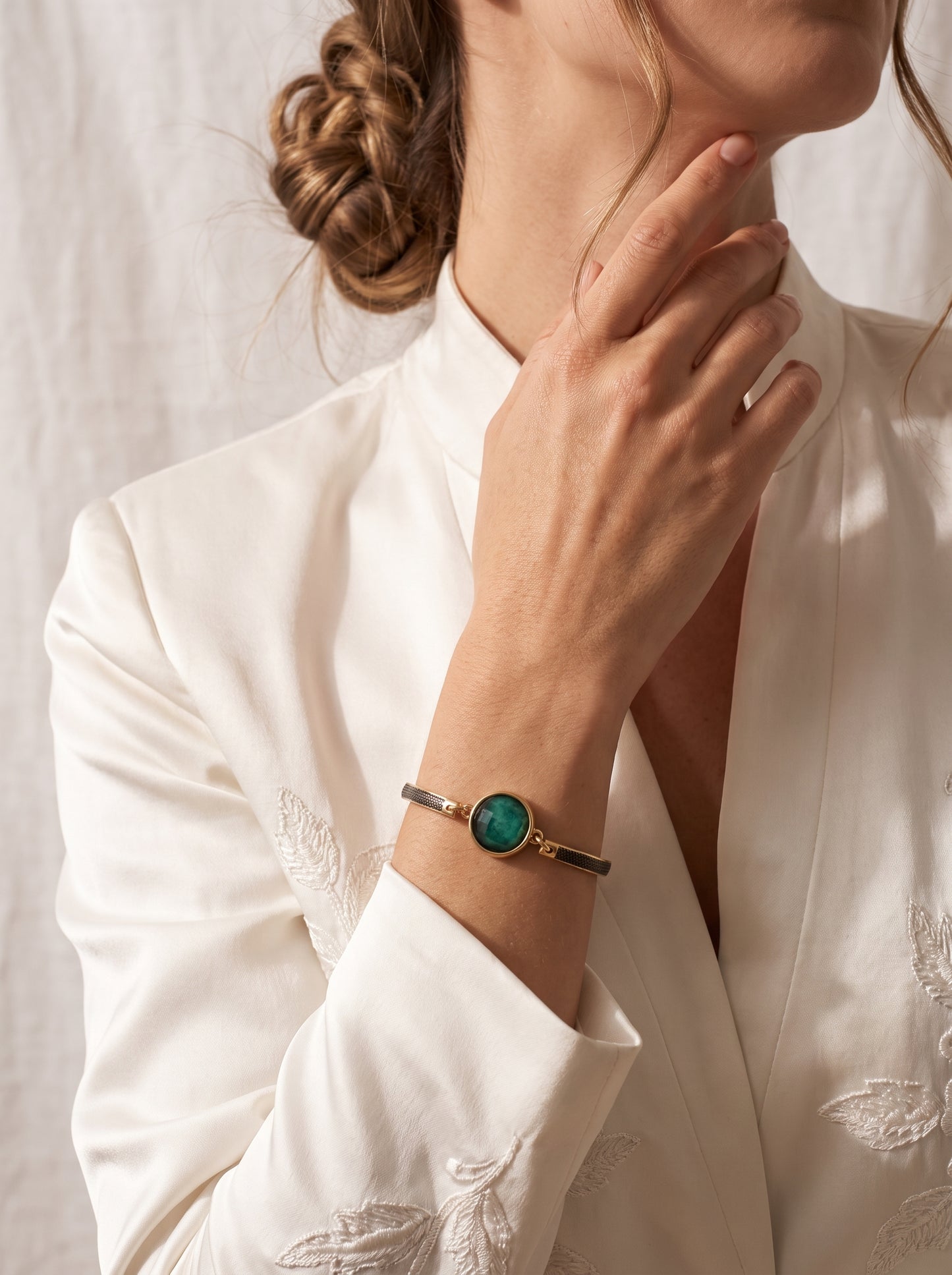 Emerald rock bracelet with gold and black rhodium-plated band worn by a woman in a white embroidered blazer