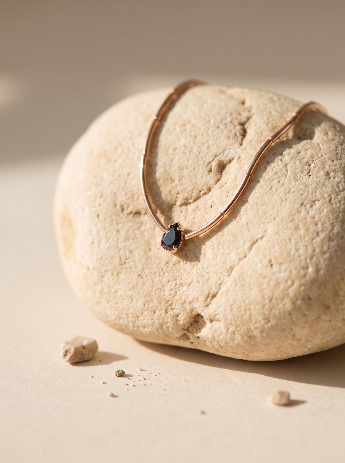 StoneCraft Jewellery gold wave chain necklace with a black teardrop crystal pendant draped over a pale textured rock.