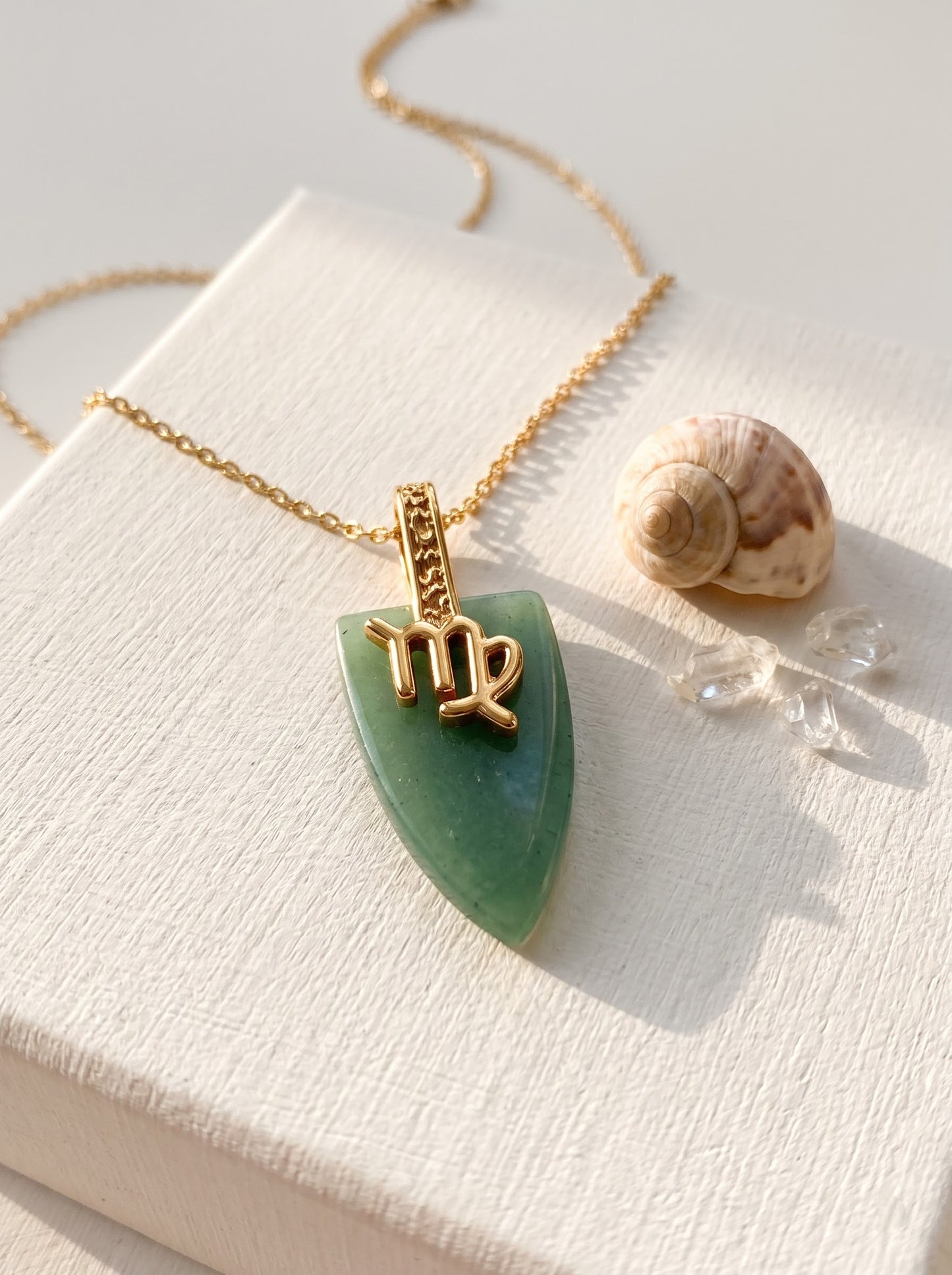 Woman wearing StoneCraft Jewellery green aventurine Virgo zodiac arrowhead pendant necklace on gold chain, cream draped fabric background.