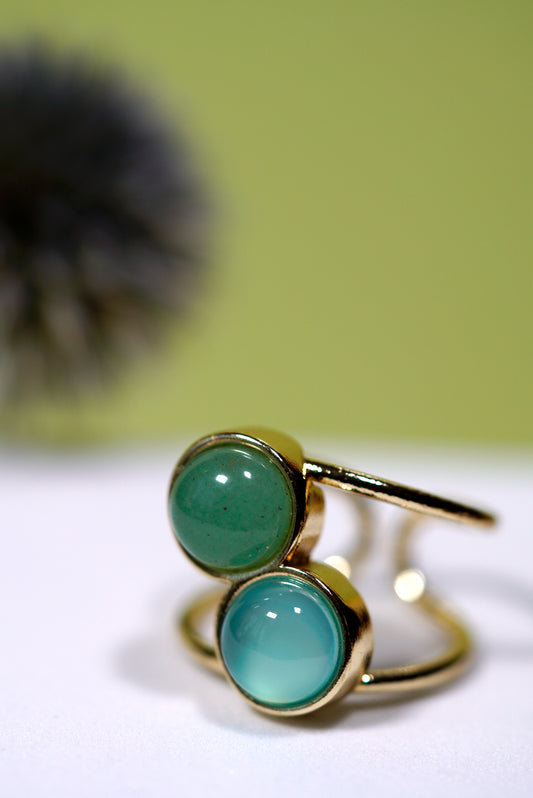 Cuff Gold ring with two round cabochon green gemstones on a white surface with a blurred background