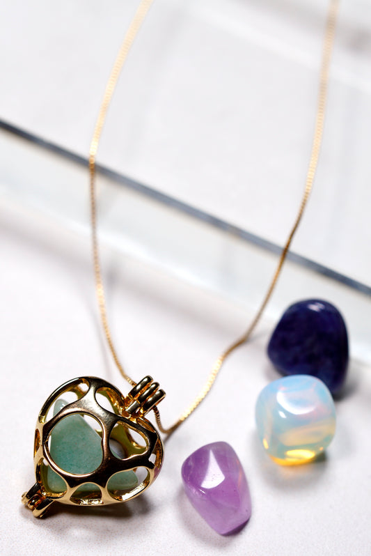 Flat lay of gold heart locket necklace with changeable gemstone set including amethyst and black onyx