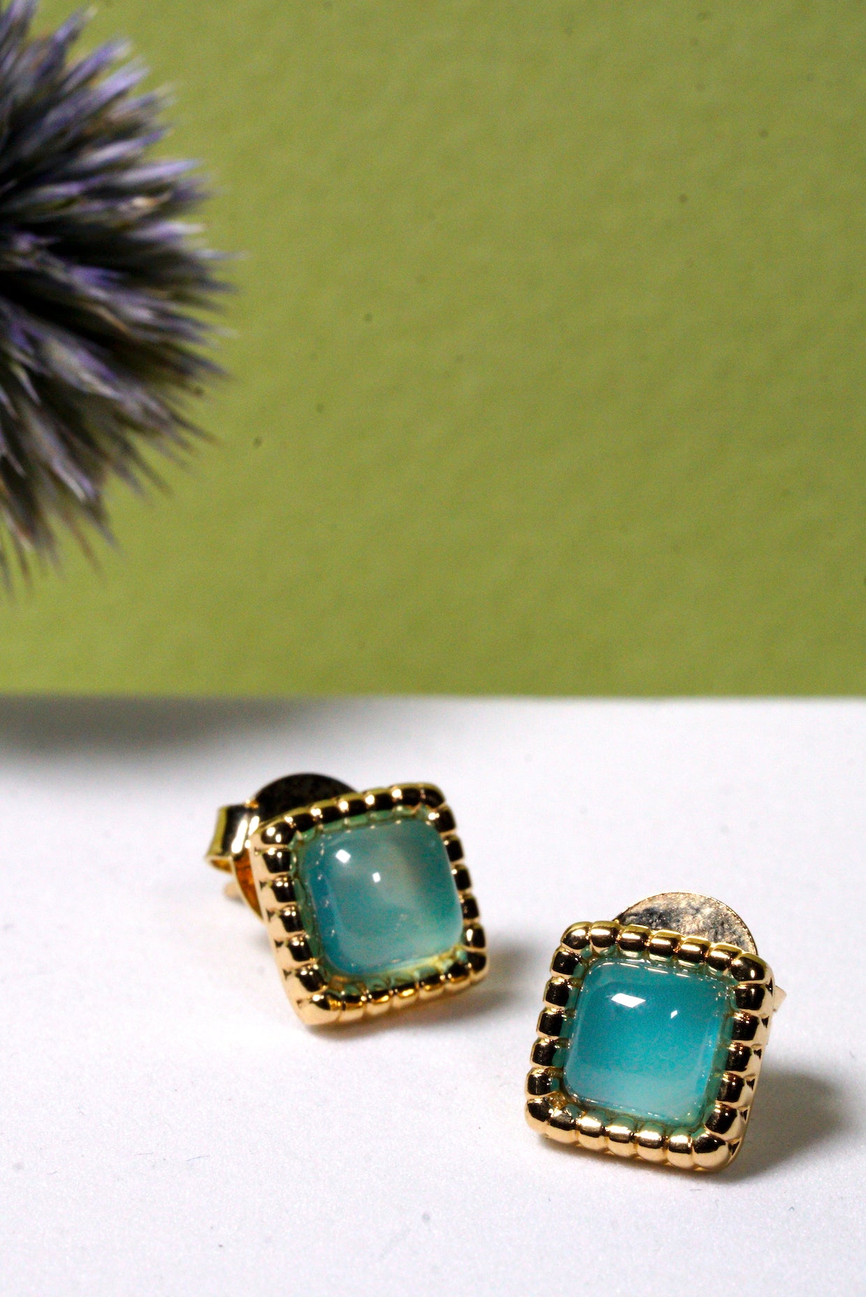 Pair of gold-framed hammered aqua agate gemstone square stud earrings on a white surface with a green background.