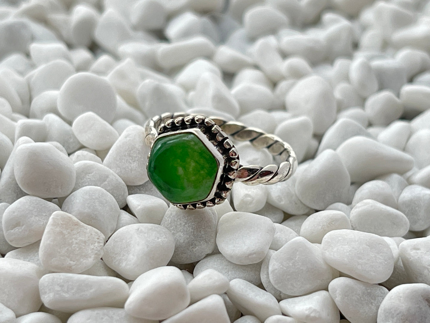 Silver ring with a green jade gemstone on white pebbles