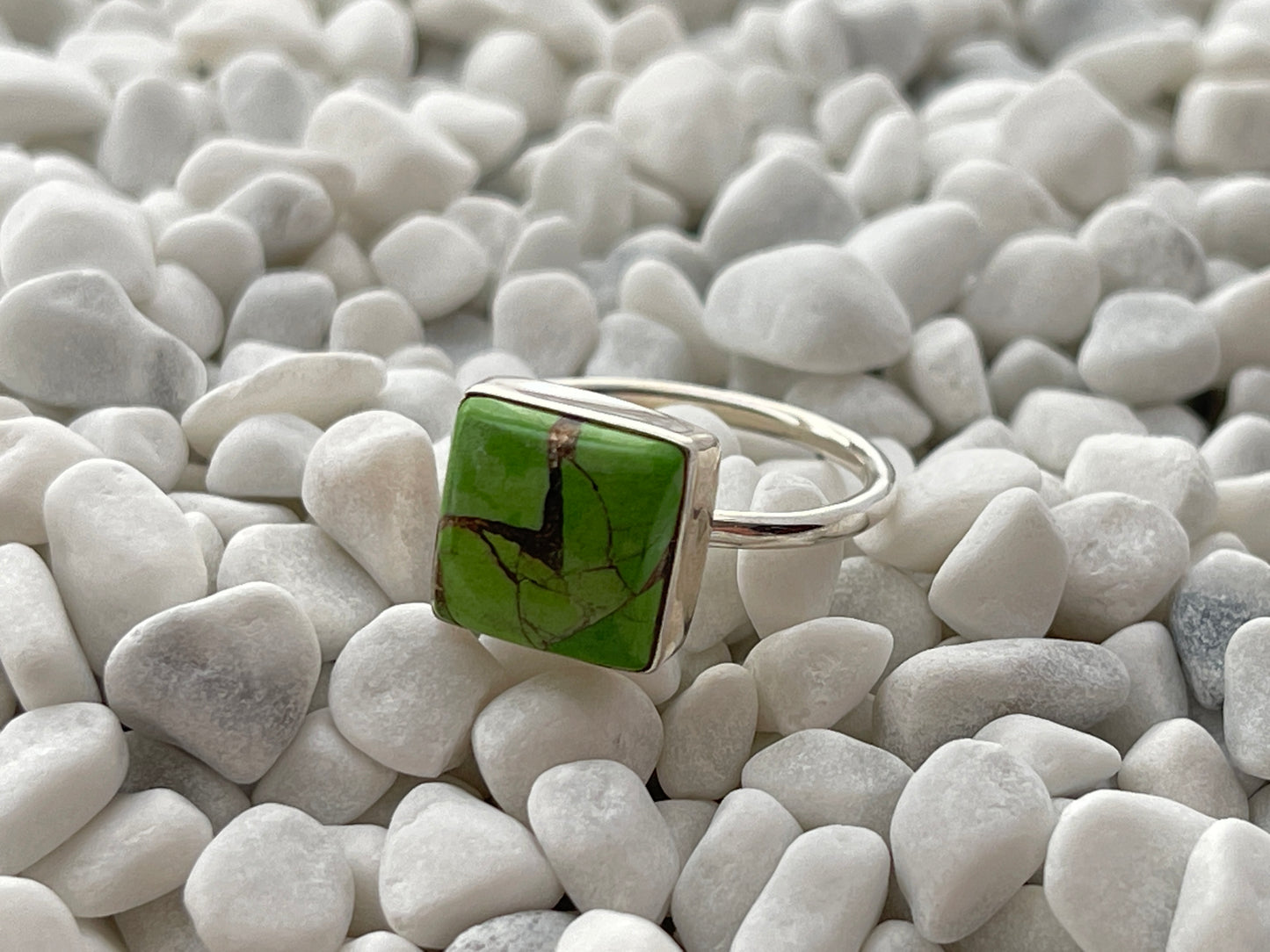 Silver ring with a green cooper turquoise gemstone on a bed of white pebbles
