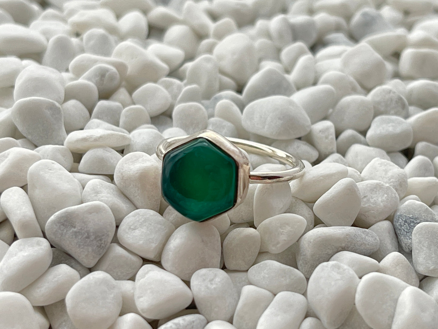 Ring with a green onyx gemstone on a bed of white pebbles