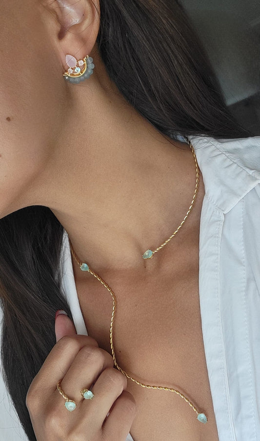 Close-up of a person wearing a twisted delicate gold necklace with small green gemstones.