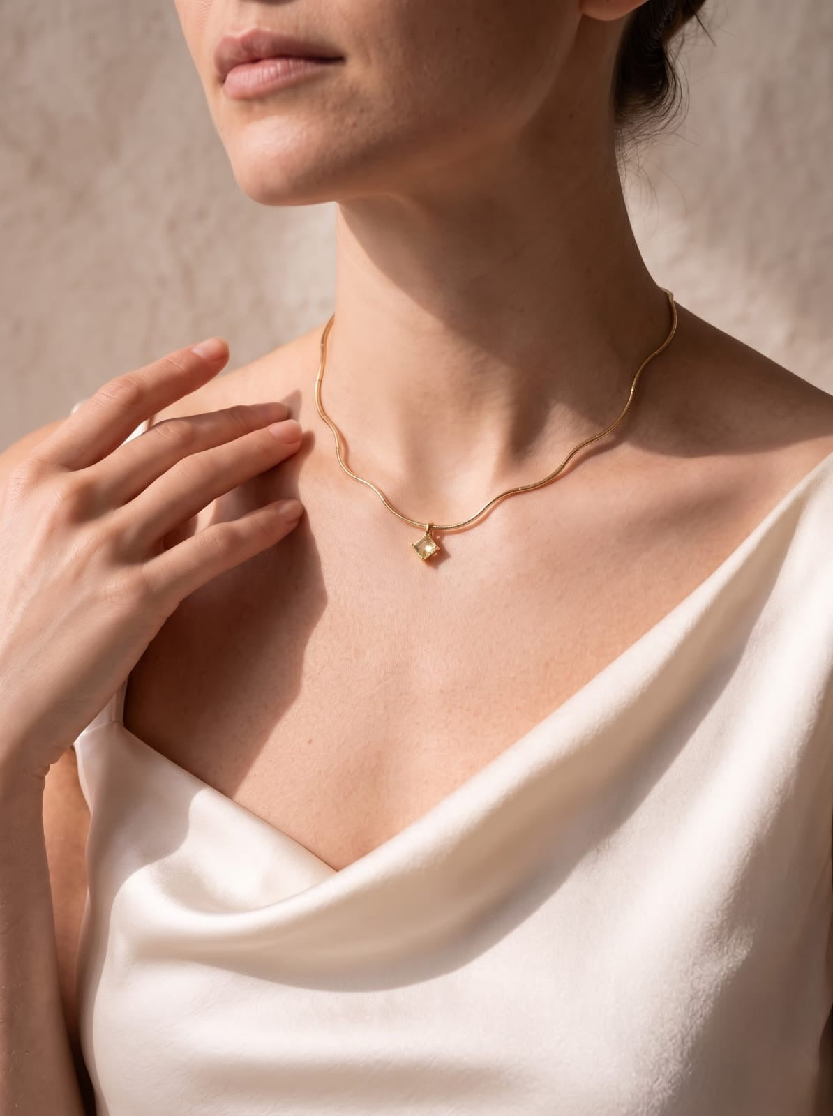 Woman wearing a StoneCraft Jewellery gold wave chain necklace with a pale yellow crystal pendant and a cream blouse.