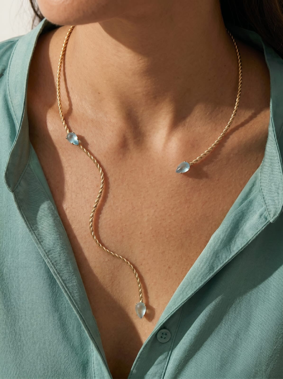 Twisted gold-plated collar necklace worn at neckline, sculptural asymmetric silhouette