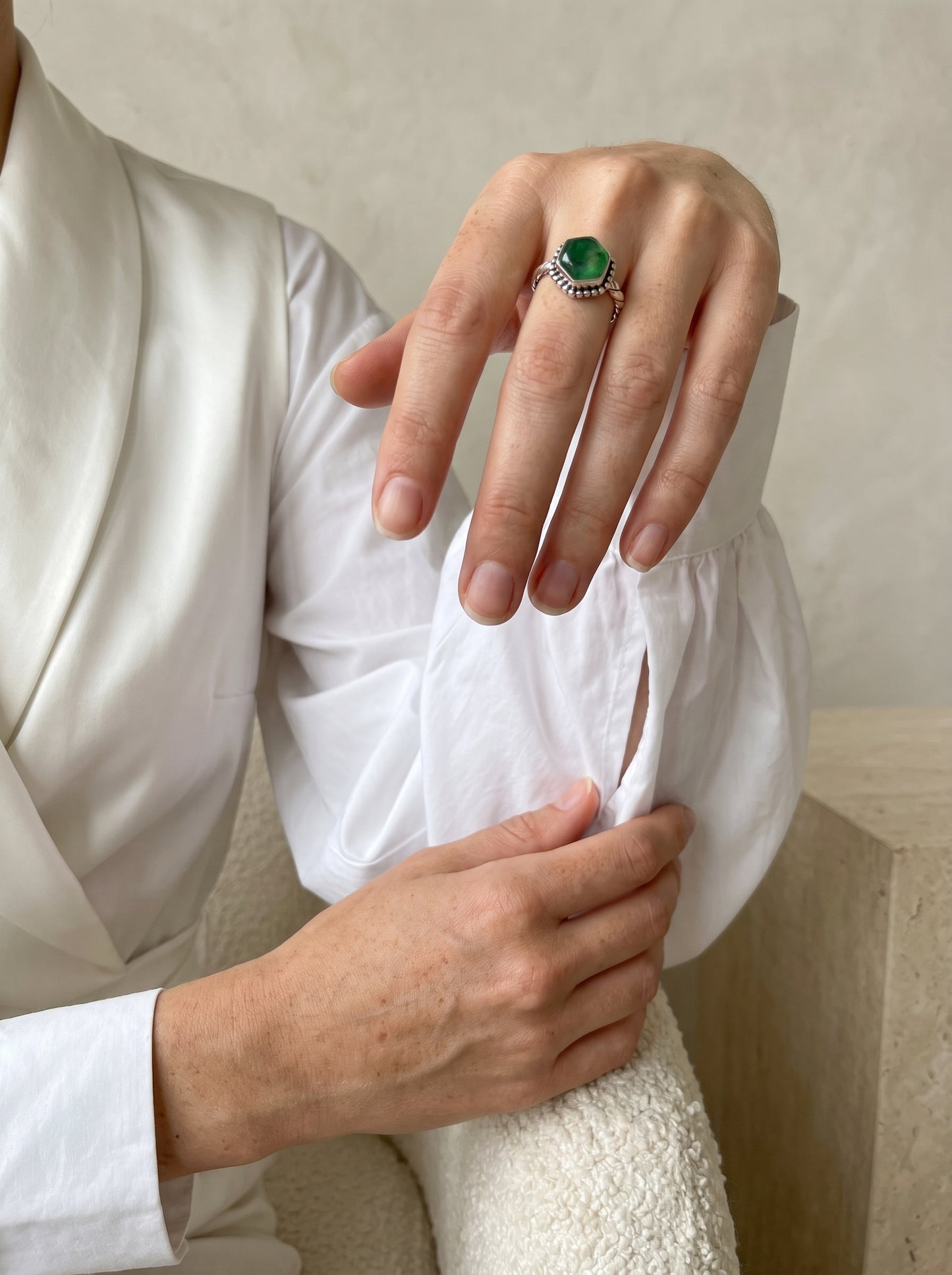 A close-up of a person wearing a silver ring with a green onyx gemstone, styled with a white satin robe and textured knit sweater.