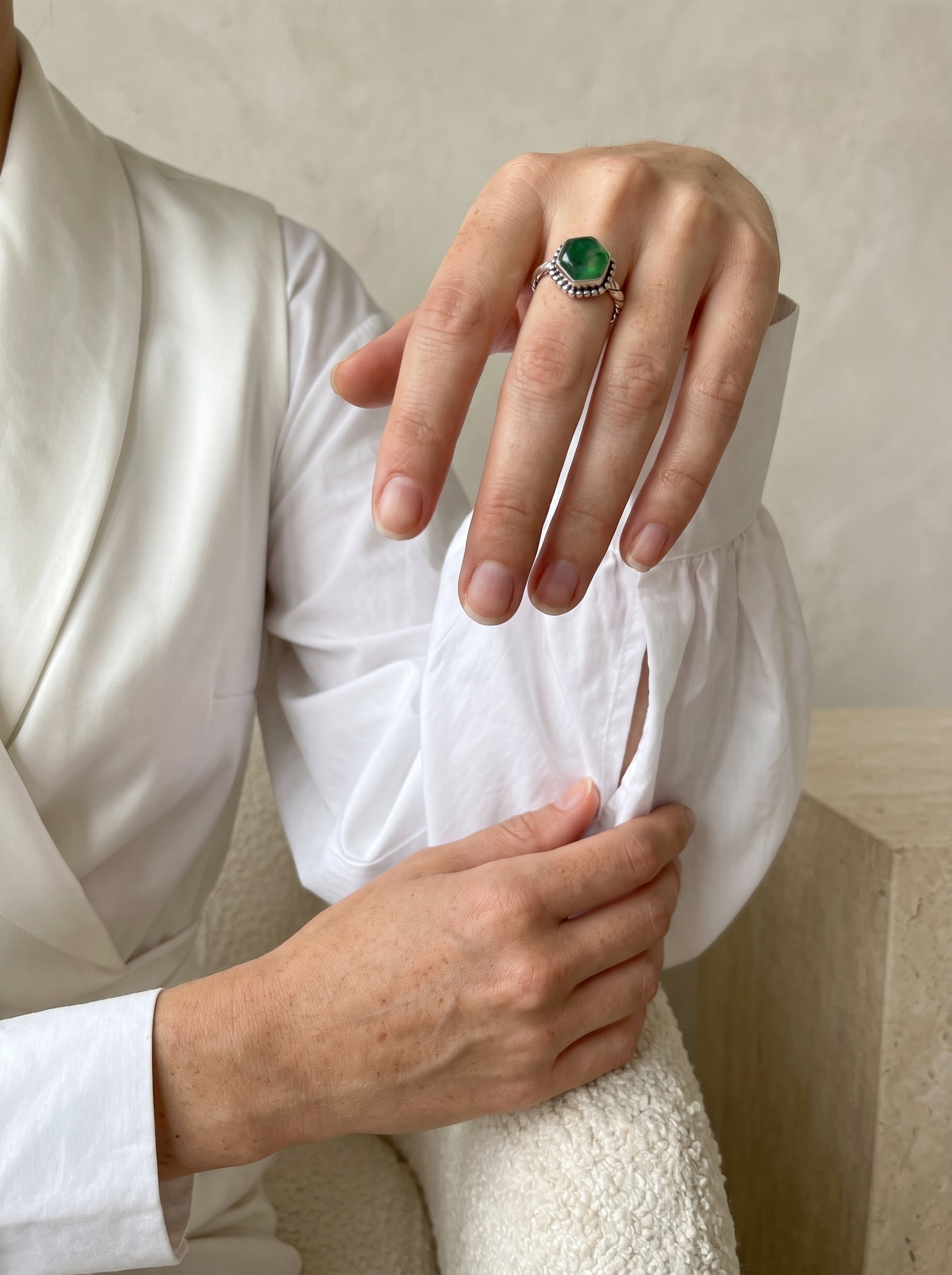 A close-up of a person wearing a silver ring with a green onyx gemstone, styled with a white satin robe and textured knit sweater.
