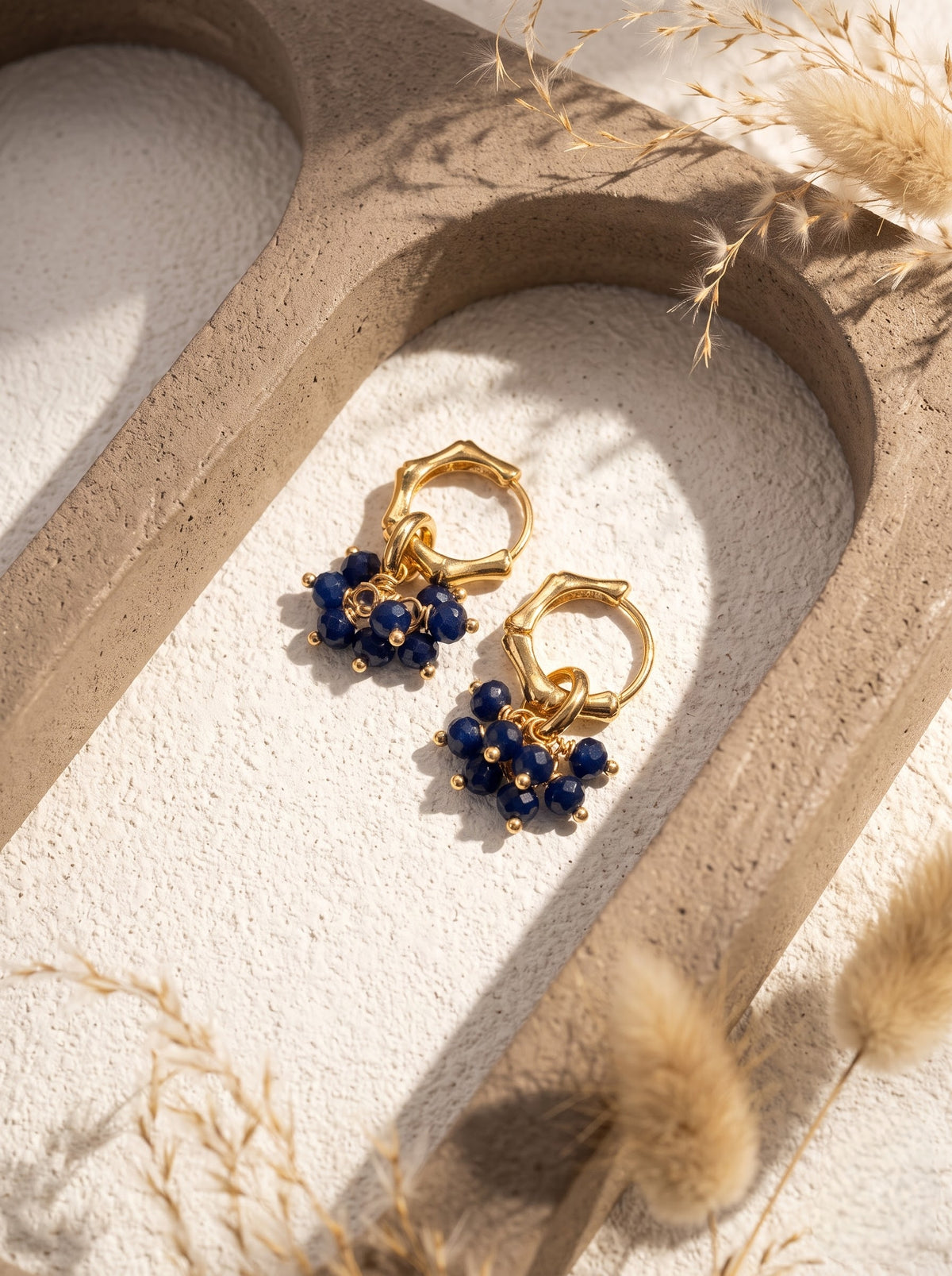 Pair of gold-plated hoop earrings with lapis lazuli bead clusters hanging on a white display branch, StoneCraft Jewellery