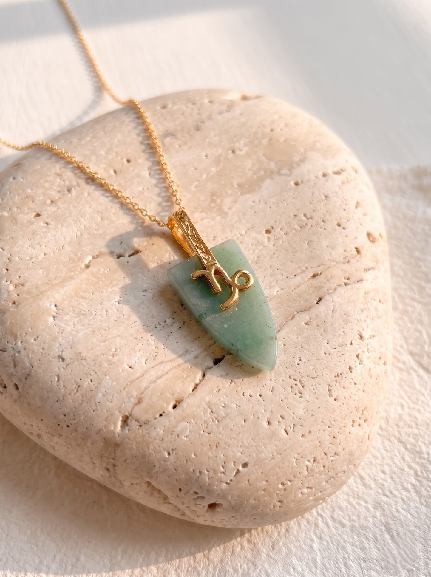 Woman wearing StoneCraft Jewellery green aventurine Capricorn zodiac arrowhead pendant necklace on gold chain, draped white top styling.
