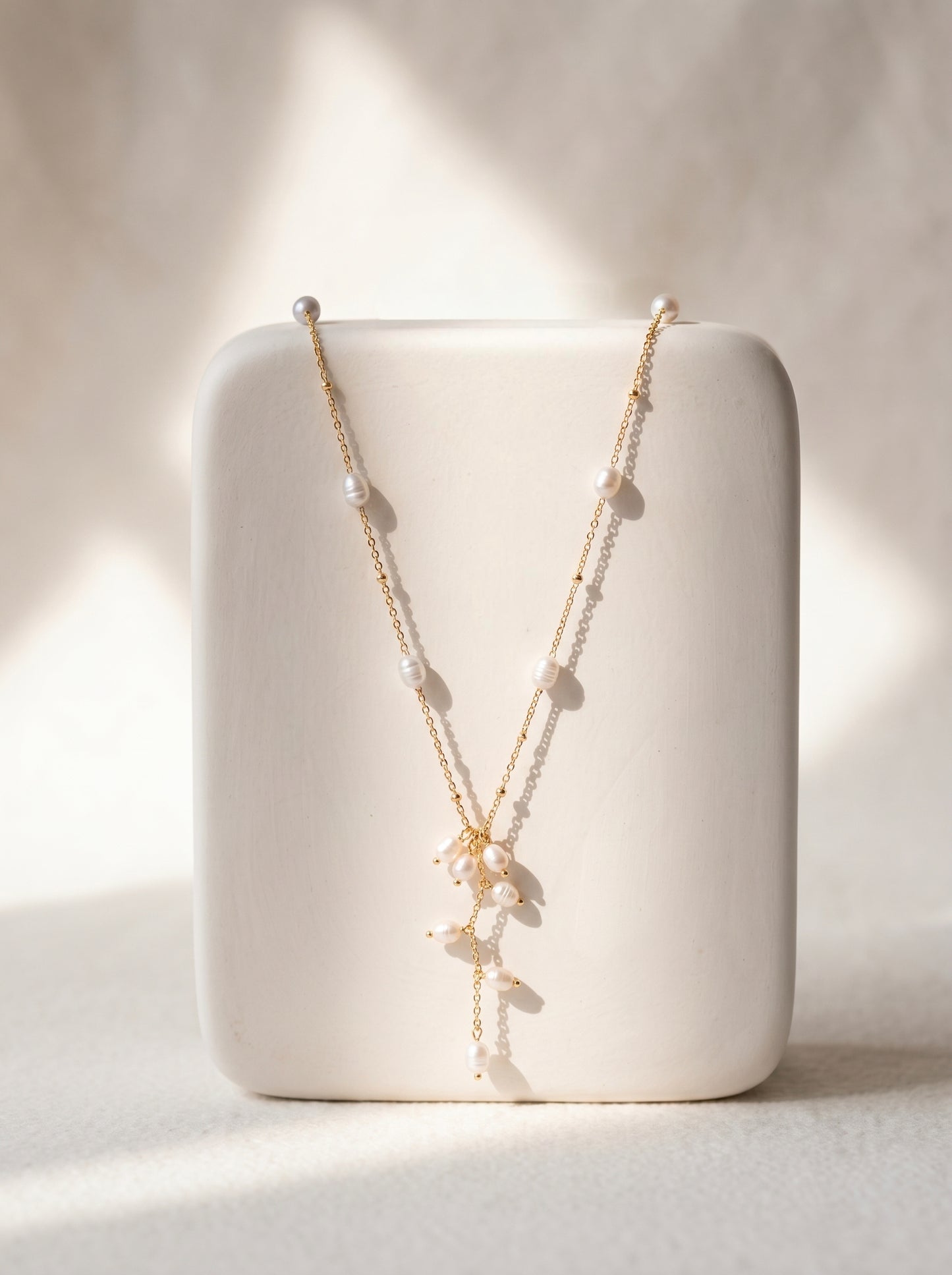 Long gold-plated freshwater pearl lariat necklace with scattered pearls and cascading pearl drop pendant on white background