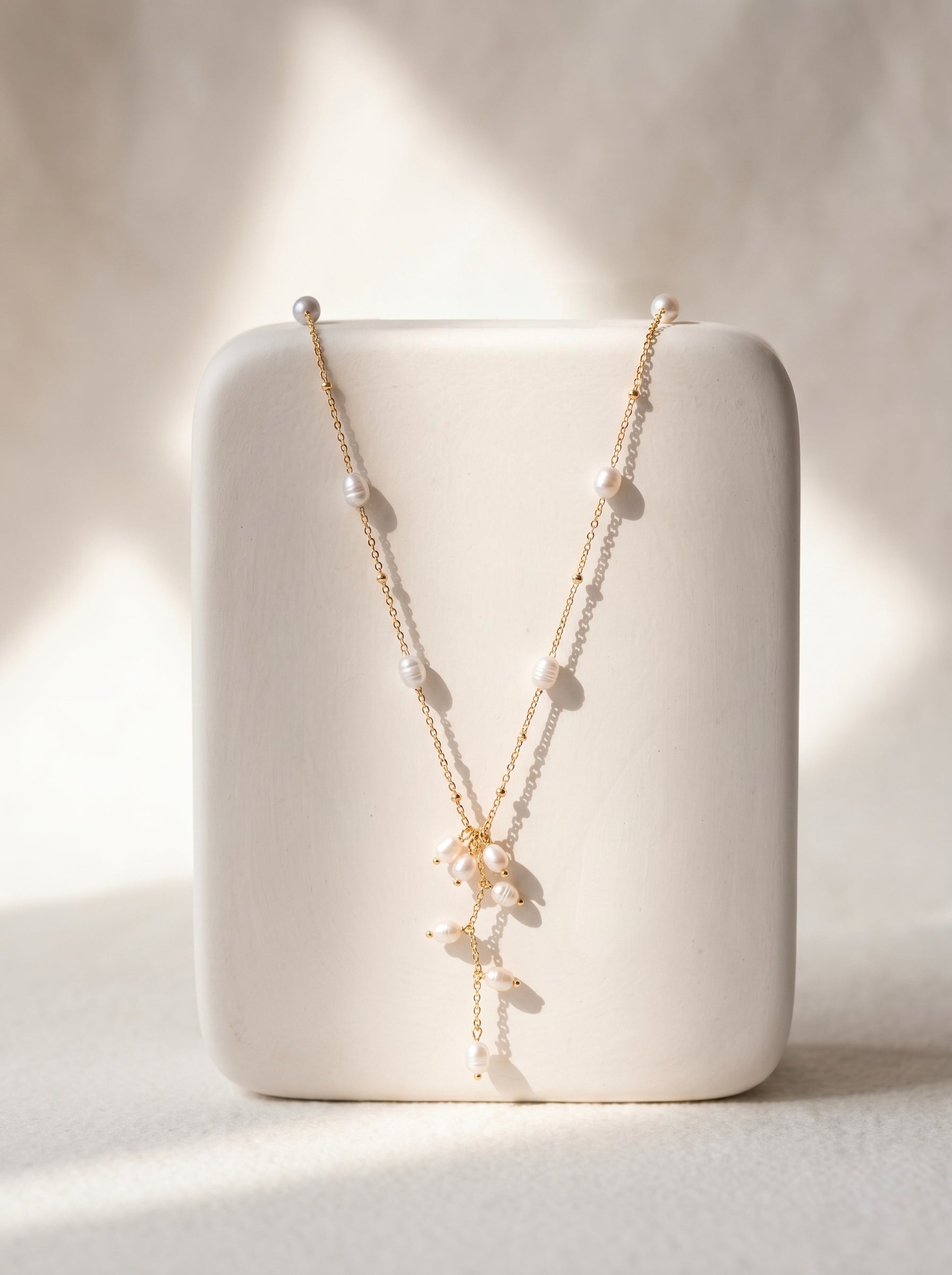 Long gold-plated freshwater pearl lariat necklace with scattered pearls and cascading pearl drop pendant on white background