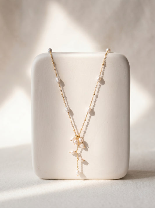 Long gold-plated freshwater pearl lariat necklace with scattered pearls and cascading pearl drop pendant on white background
