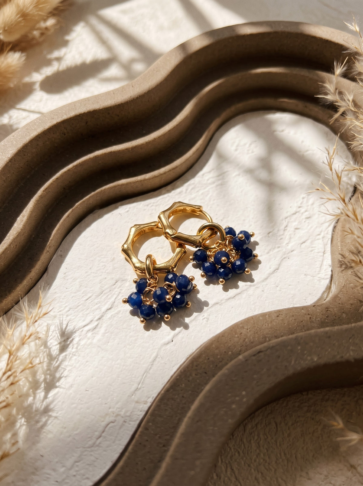 Close-up of gold-plated hoop earring with lapis lazuli bead cluster worn on a model's ear, StoneCraft Jewellery