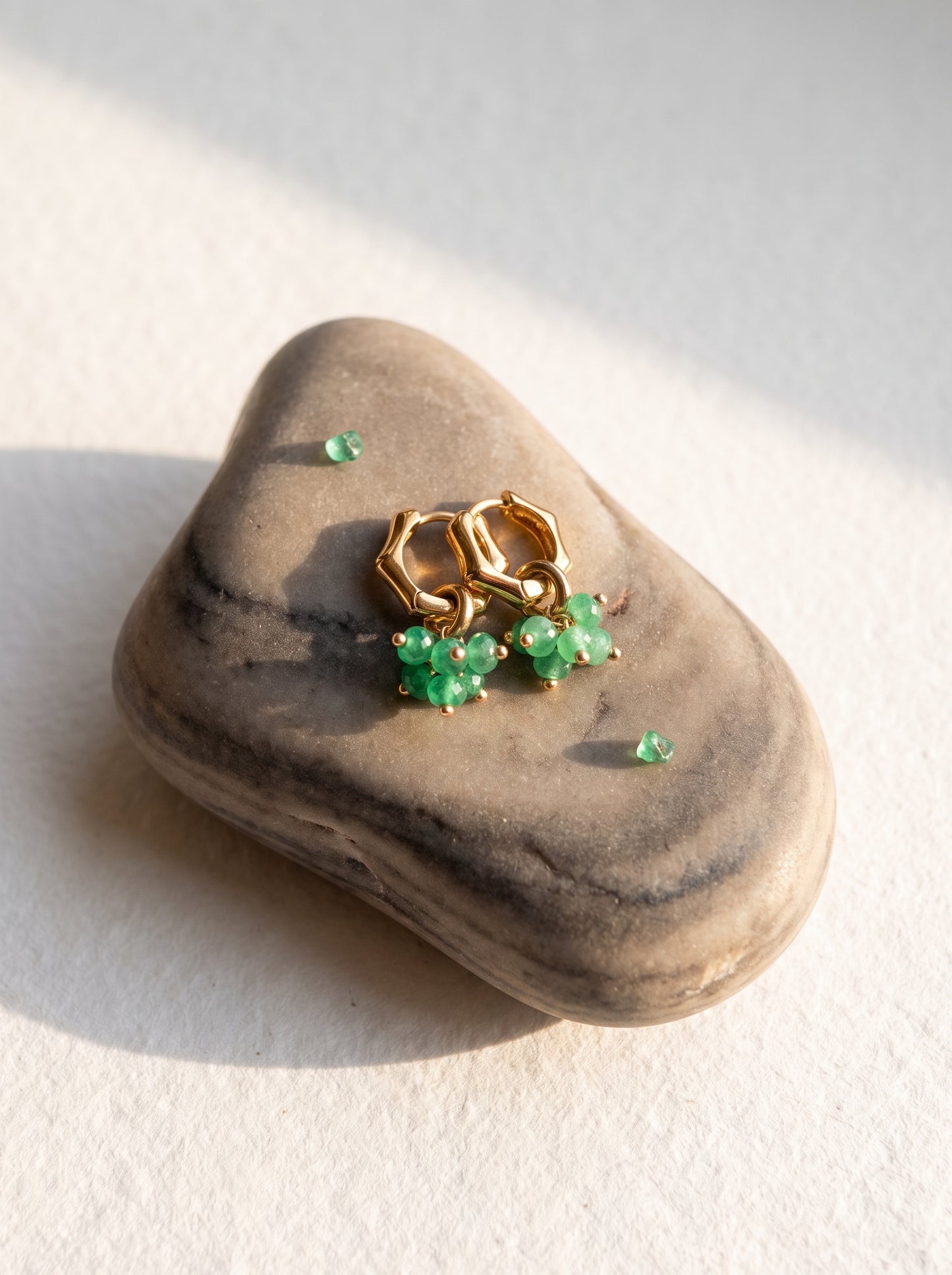 Pair of green jade hoop earrings with gold cluster charm resting on a natural stone"