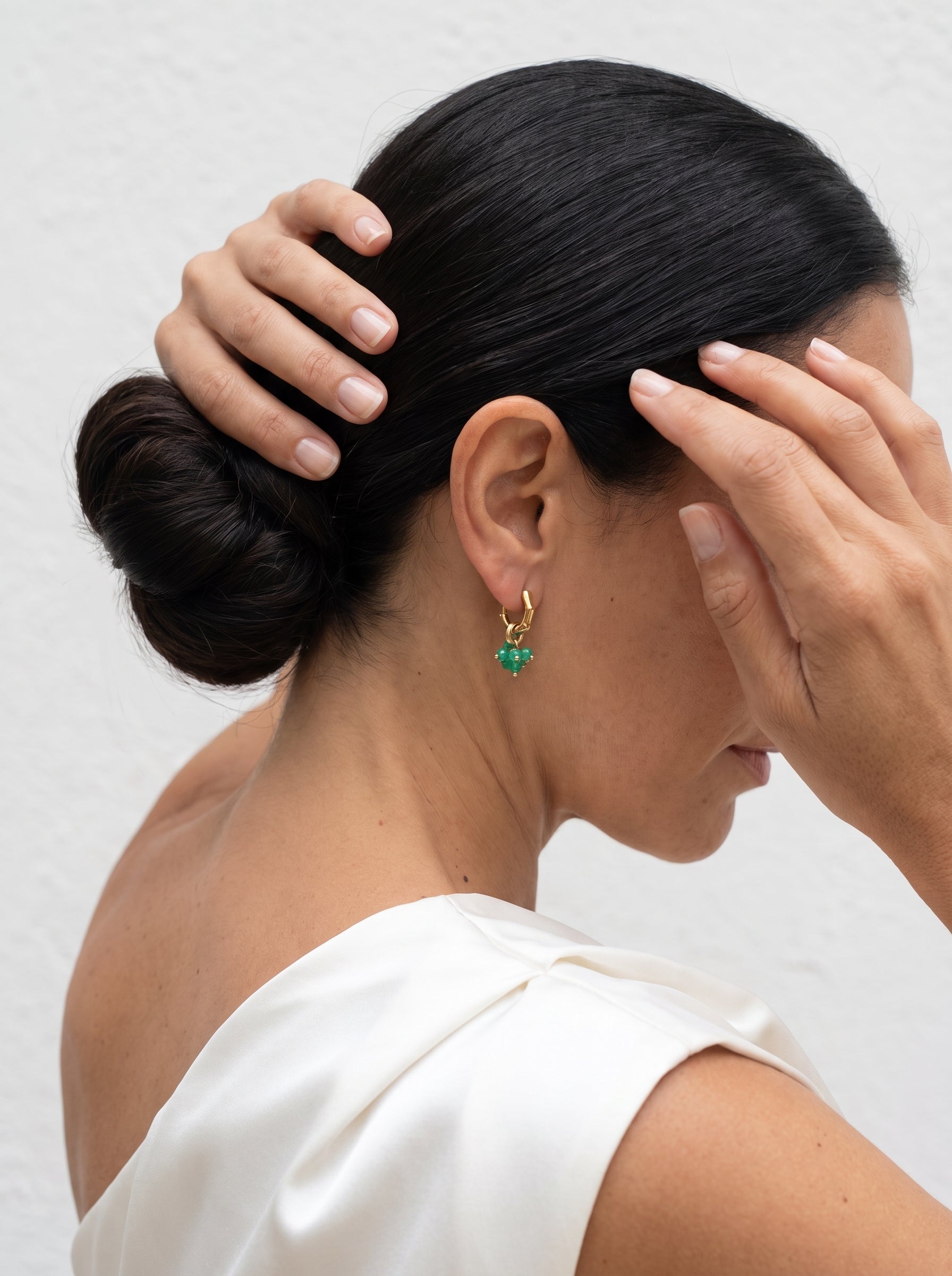 Close-up of green jade cluster hoop earring worn by model with dark hair in a bun