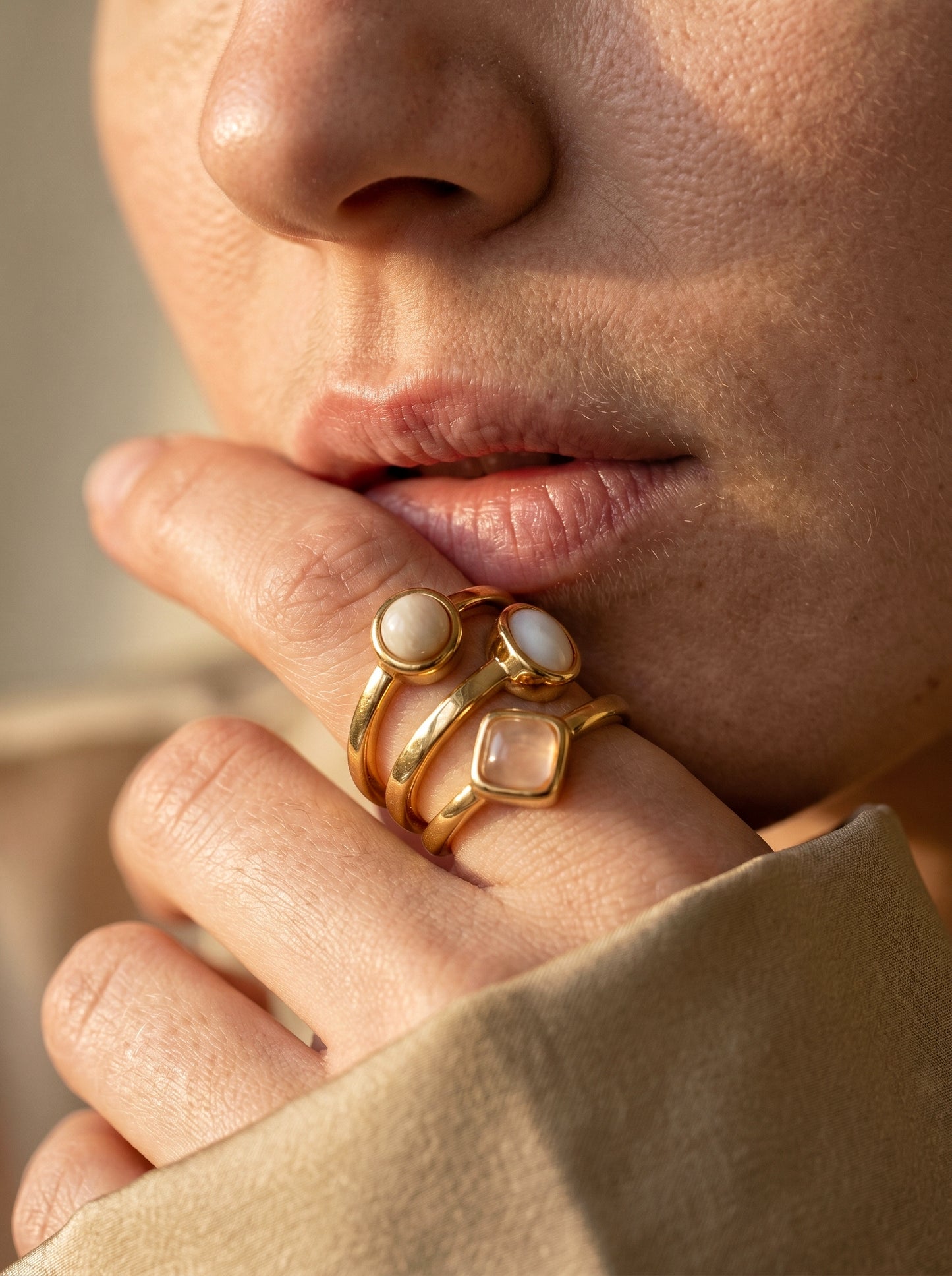 Close-up of model wearing gold multi-stone ring with mother of pearl and rose quartz stones, hand raised near face