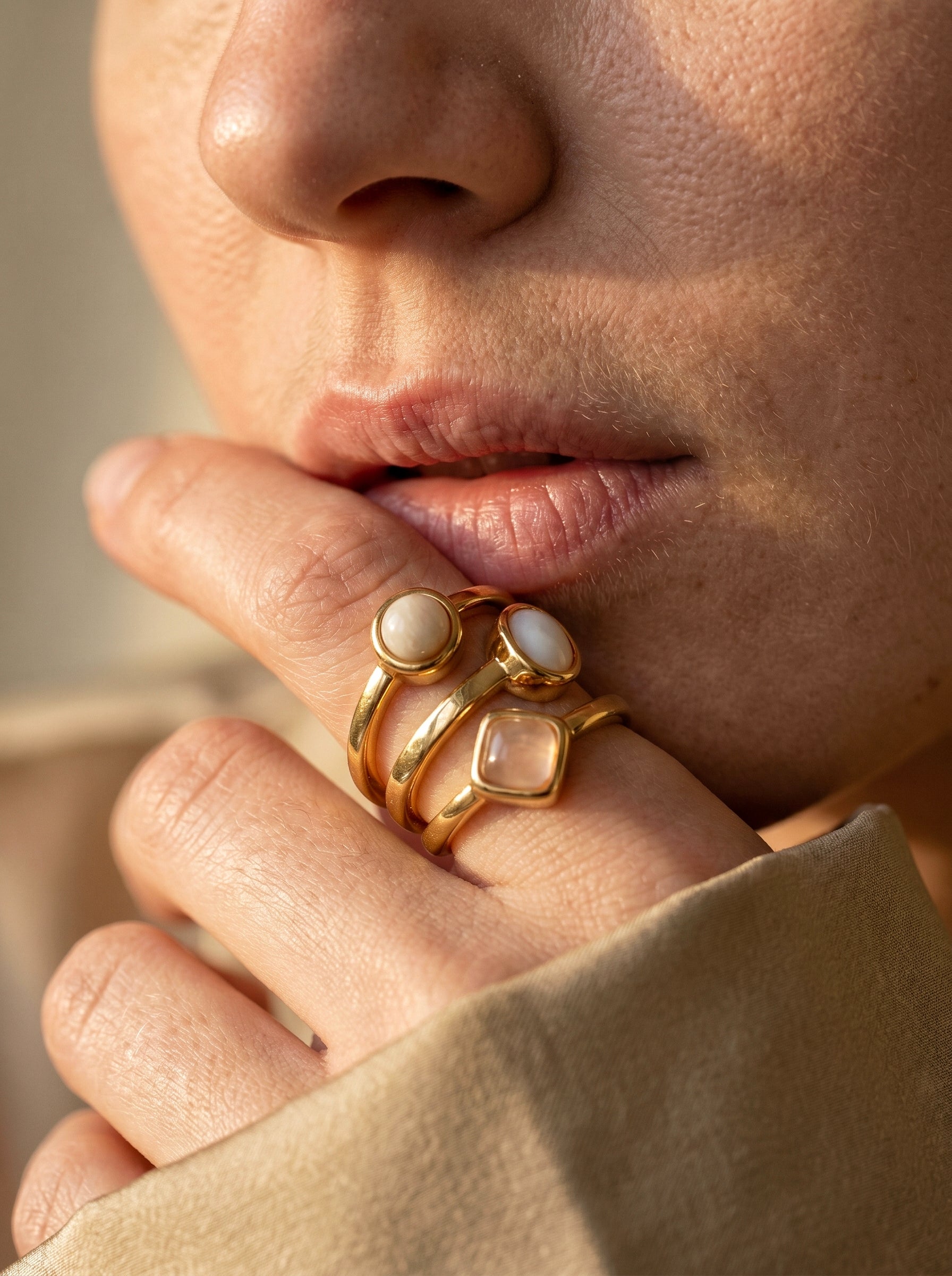 Close-up of model wearing gold multi-stone ring with mother of pearl and rose quartz stones, hand raised near face