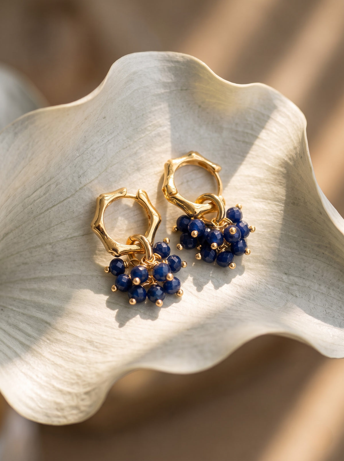 Pair of gold-plated hoop earrings with lapis lazuli bead clusters lying flat on a light surface, StoneCraft Jewellery