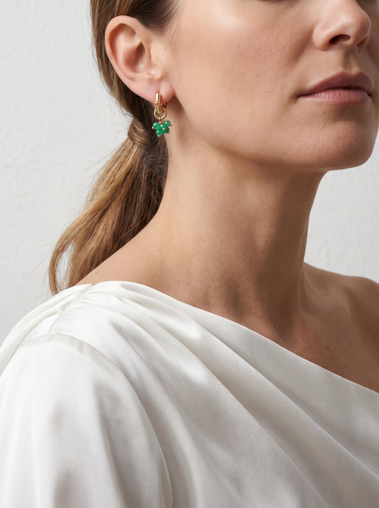 Woman wearing green jade hoop earrings with gold cluster charm, side profile view"