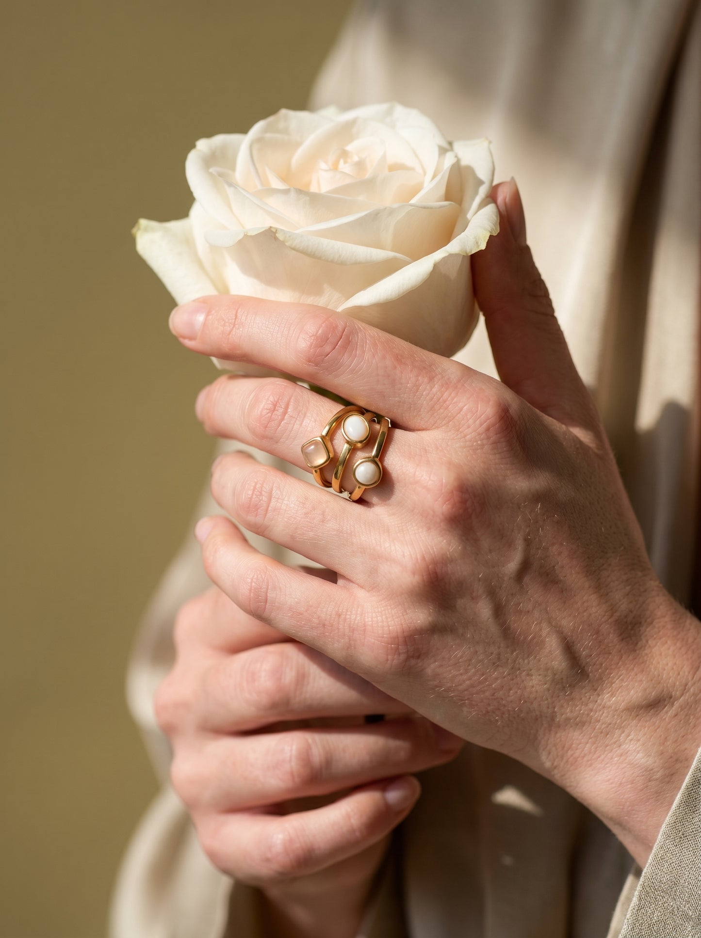 Close-up of model wearing gold multi-stone ring with mother of pearl and rose quartz stones, hand raised near face