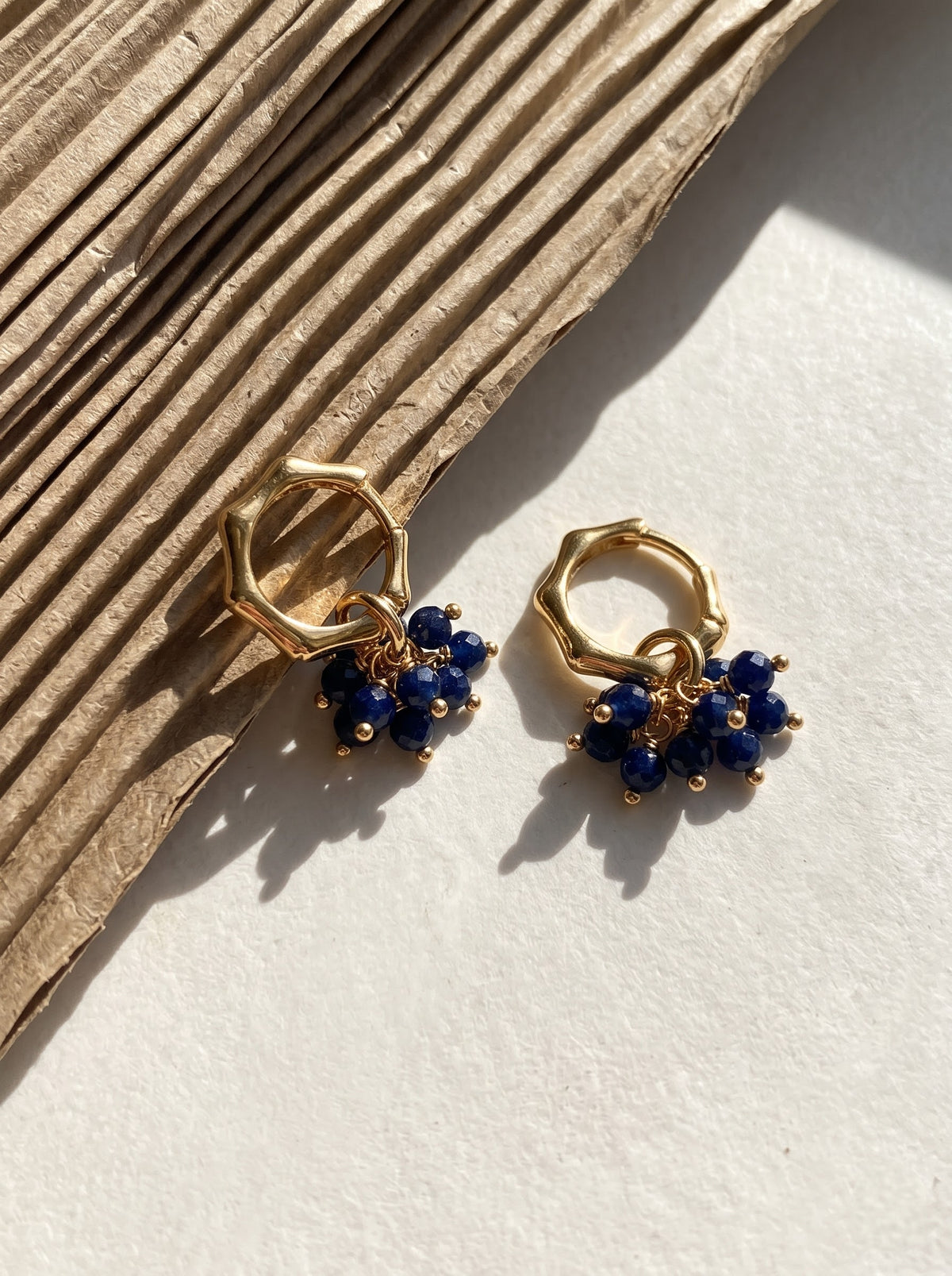 Close-up of gold-plated hoop earrings with lapis lazuli bead clusters on a light background, StoneCraft Jewellery