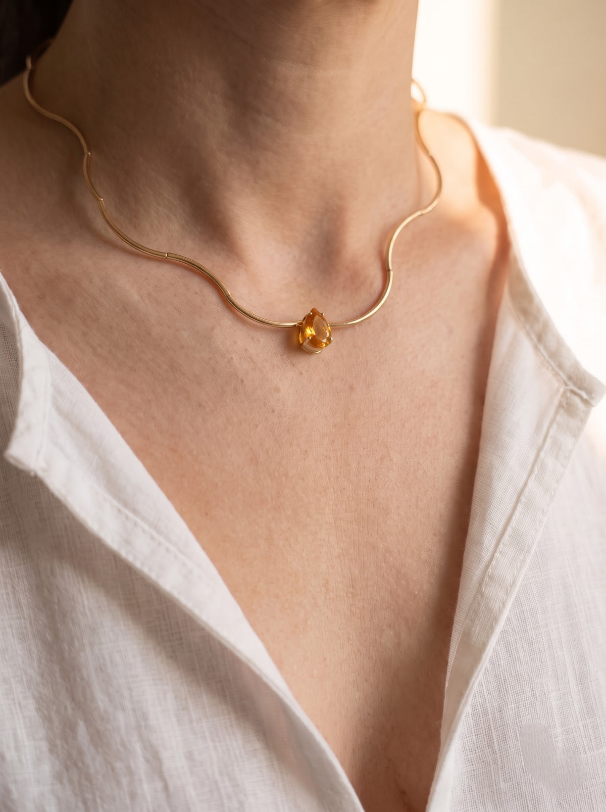 Woman wearing StoneCraft Jewellery Gold Wave Chain Necklace with orange Crystal Pendant close-up on neck with white linen shirt