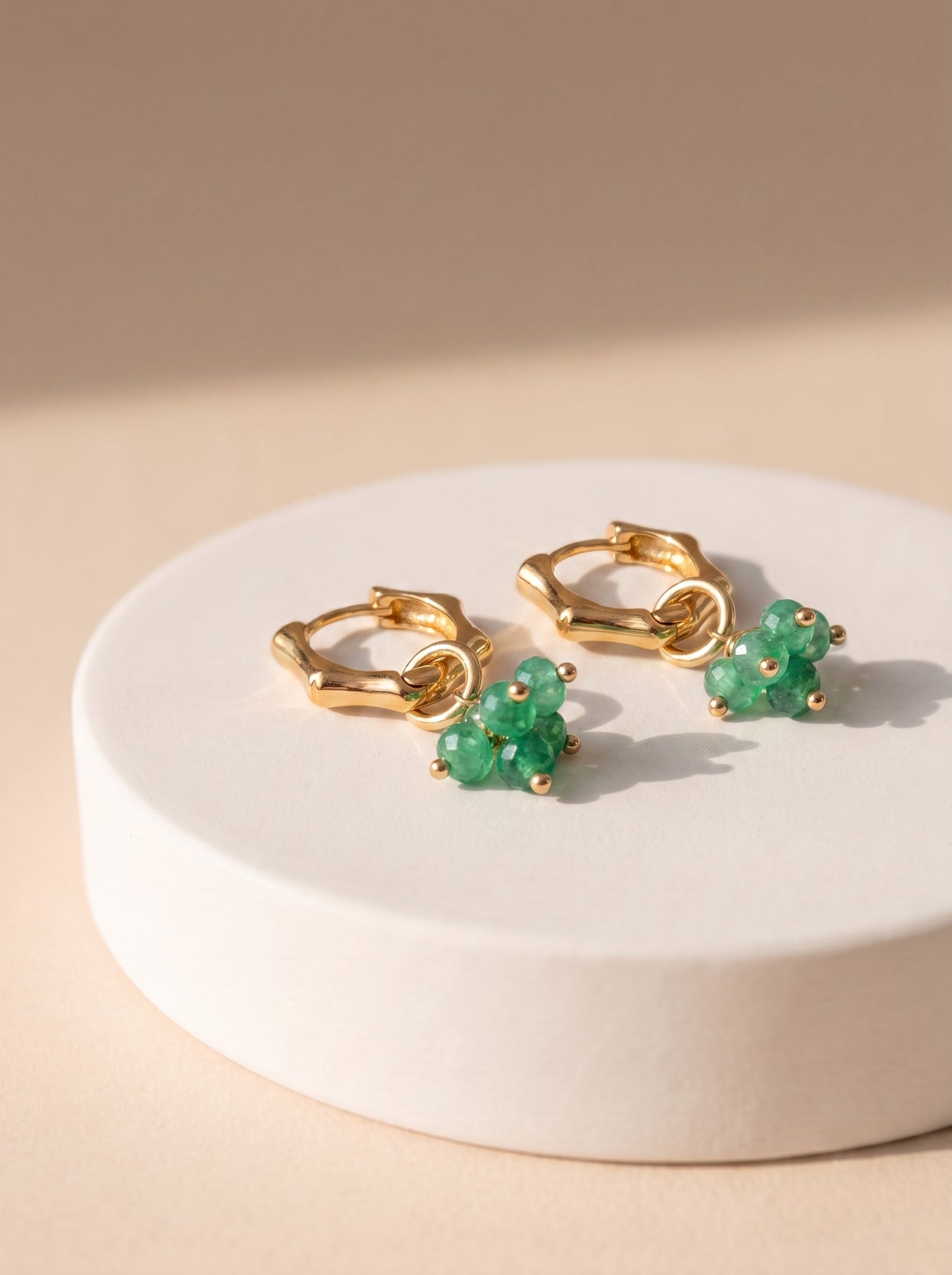 Green jade cluster hoop earrings in gold displayed on a white ceramic stand"