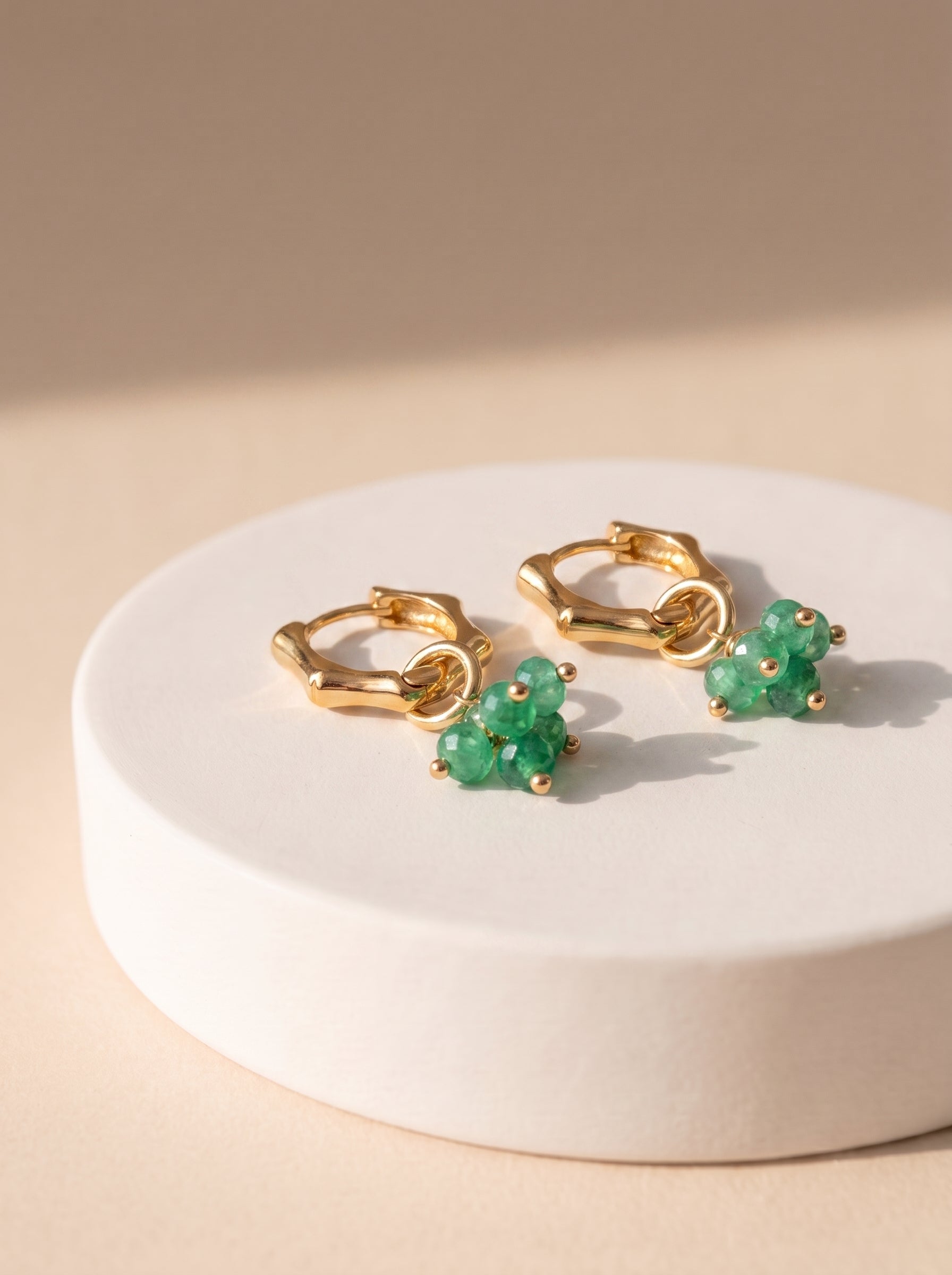 Green jade cluster hoop earrings in gold displayed on a white ceramic stand"