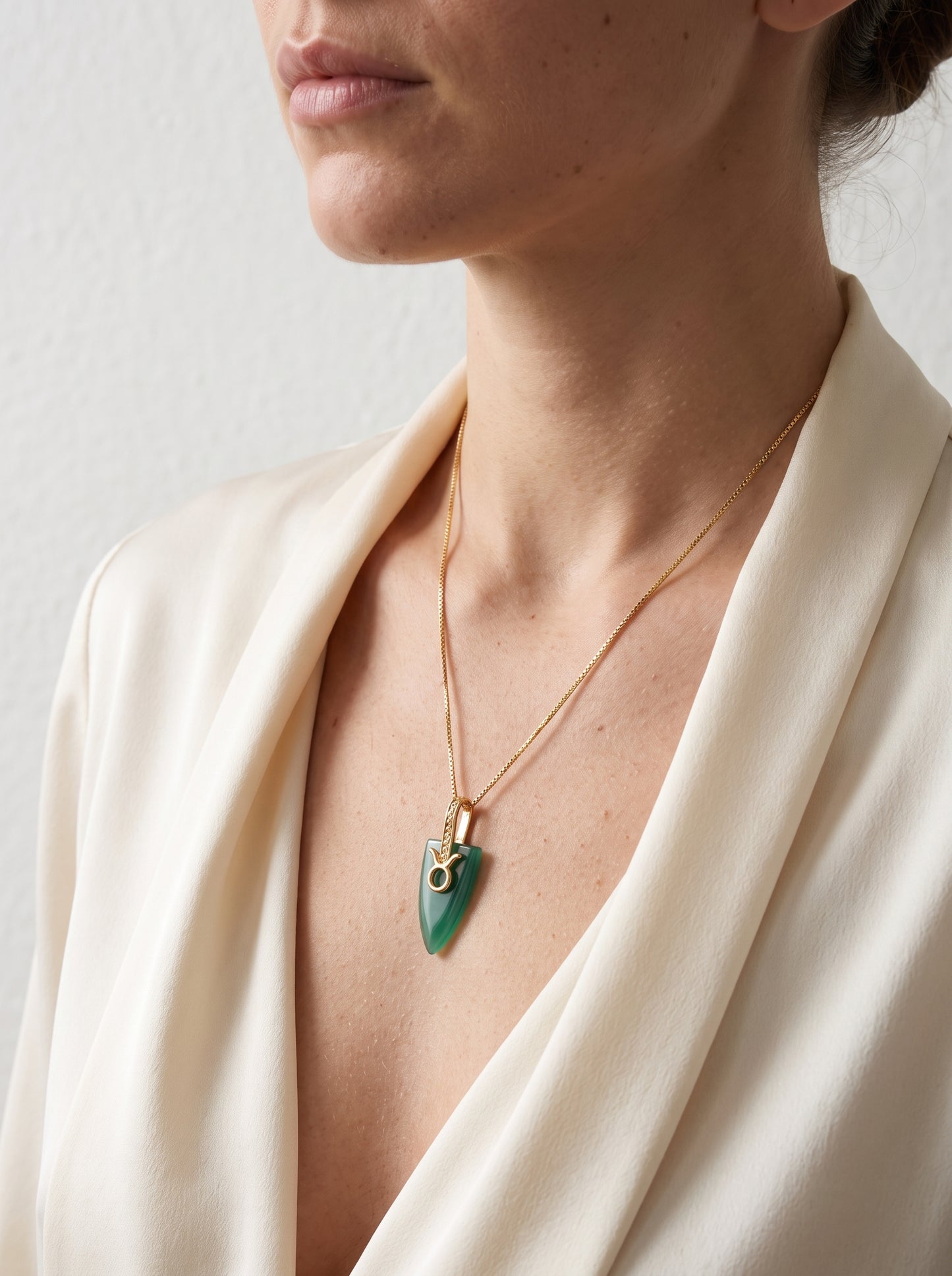 Green agate Taurus zodiac pendant necklace worn by a woman in a cream open-front blazer