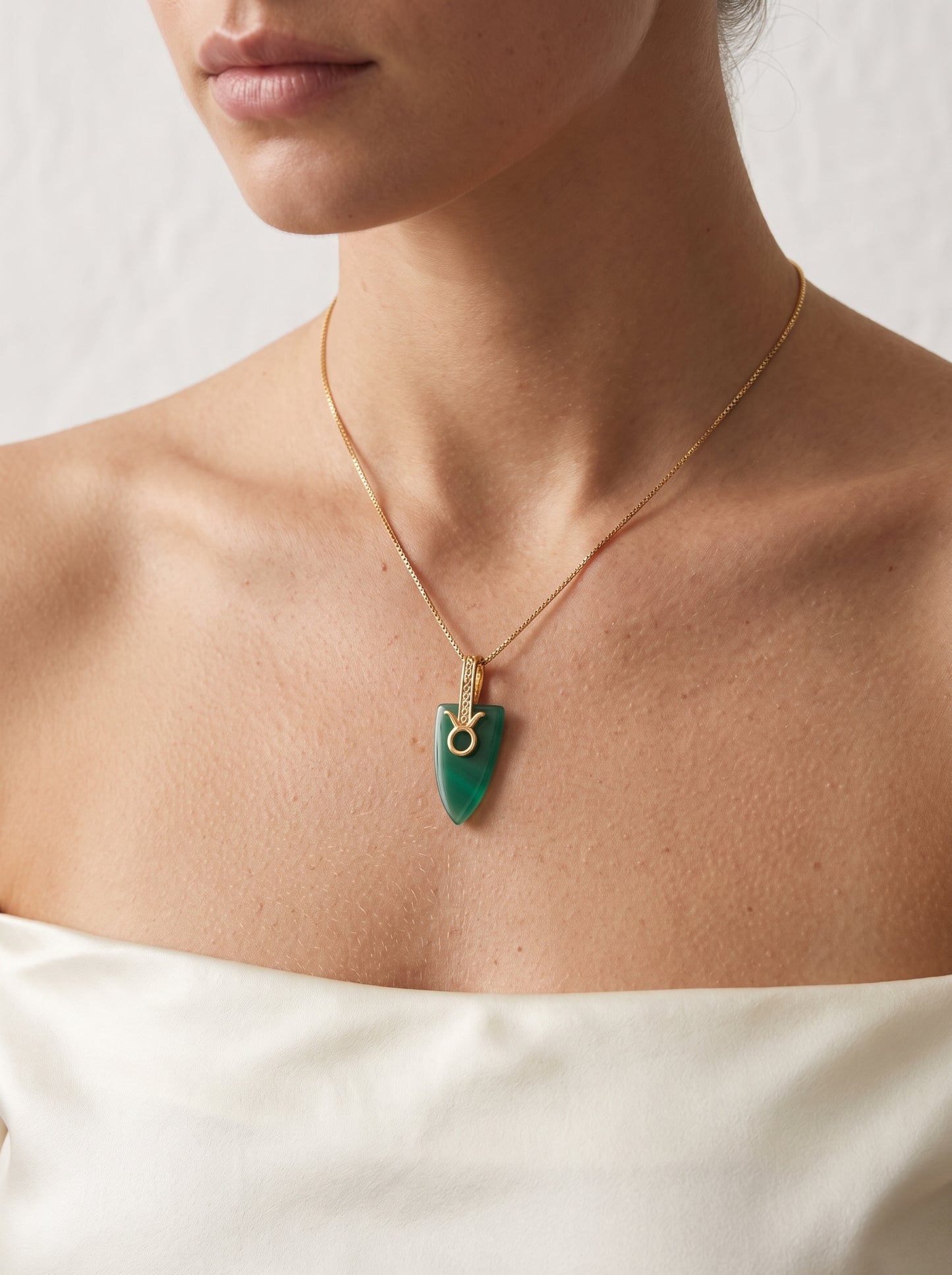 Gold-plated Taurus agate arrowhead pendant necklace worn by a woman in a white strapless top showing full collarbone
