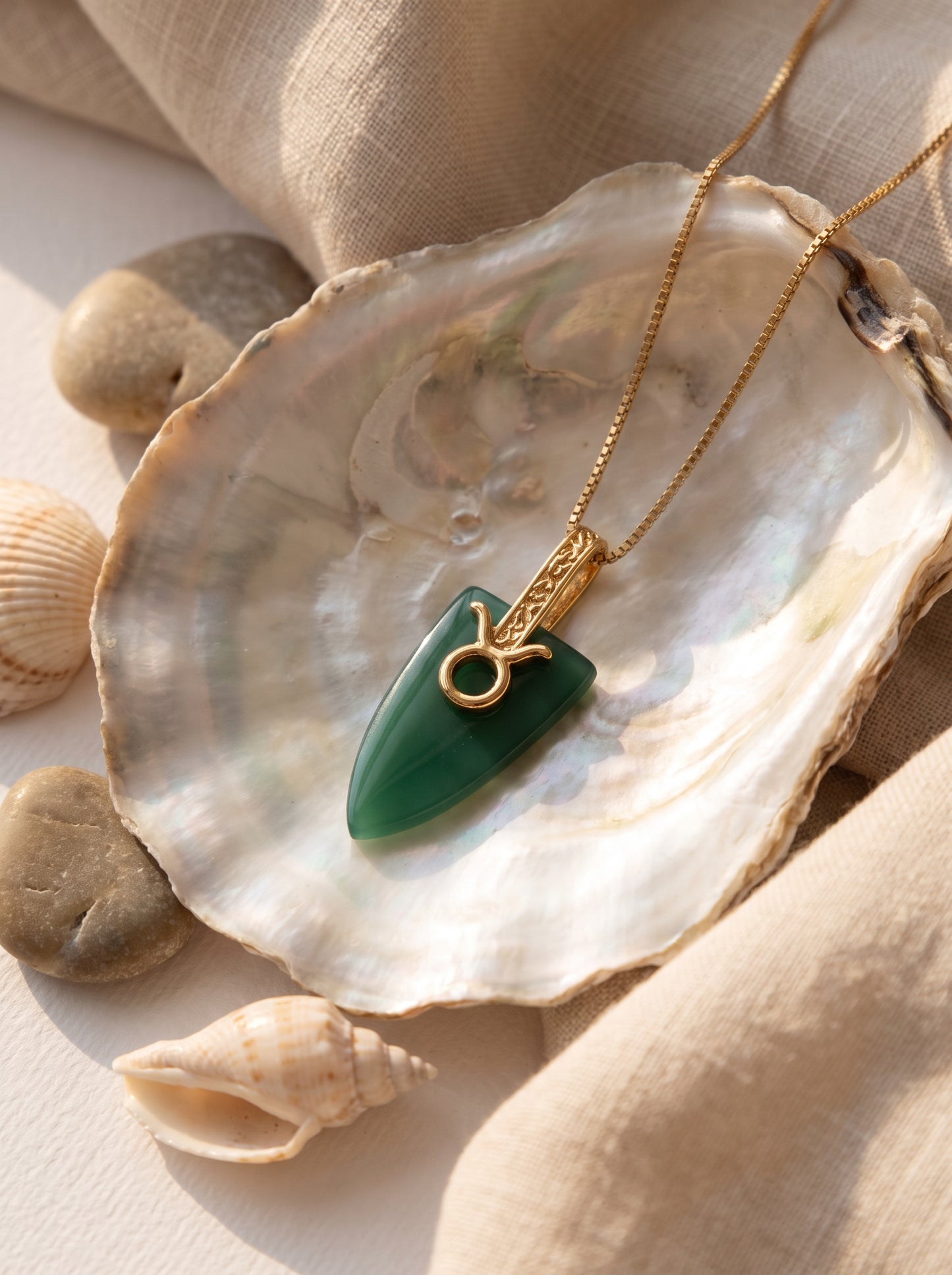 Taurus agate pendant necklace with gold Taurus symbol laid inside an oyster shell surrounded by small seashells and pebbles