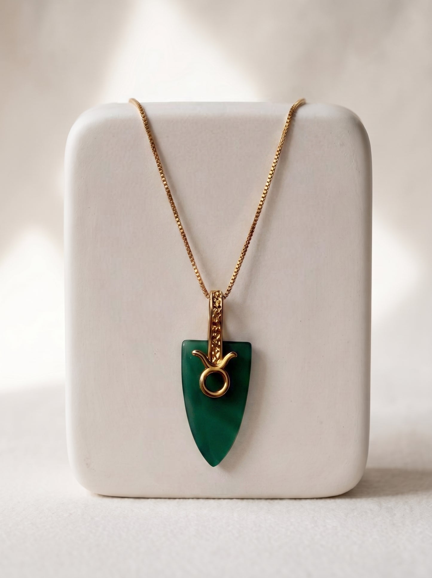 Gold-plated box chain necklace with green agate arrowhead pendant and Taurus zodiac bail displayed on a white jewellery stand