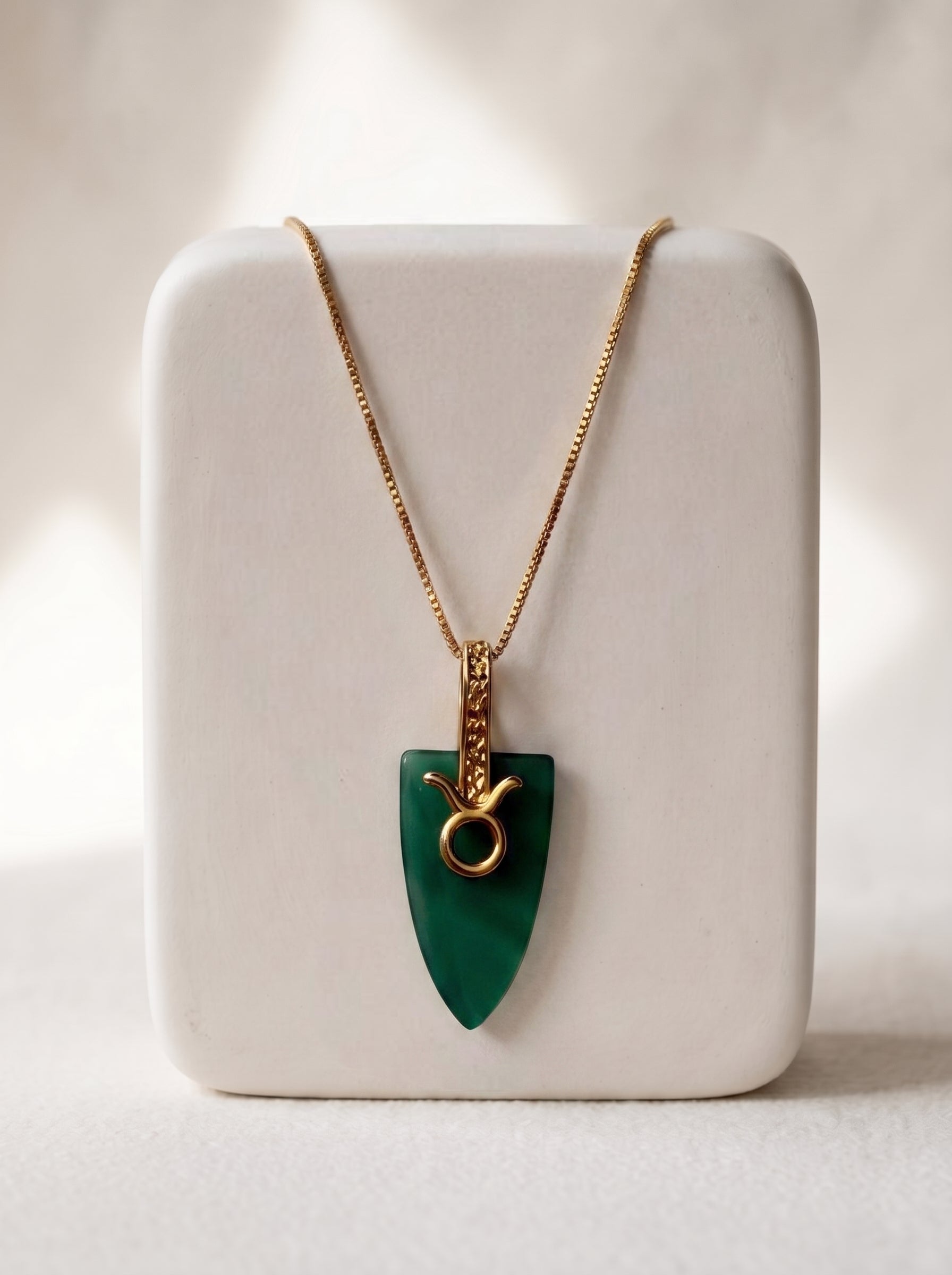 Gold-plated box chain necklace with green agate arrowhead pendant and Taurus zodiac bail displayed on a white jewellery stand