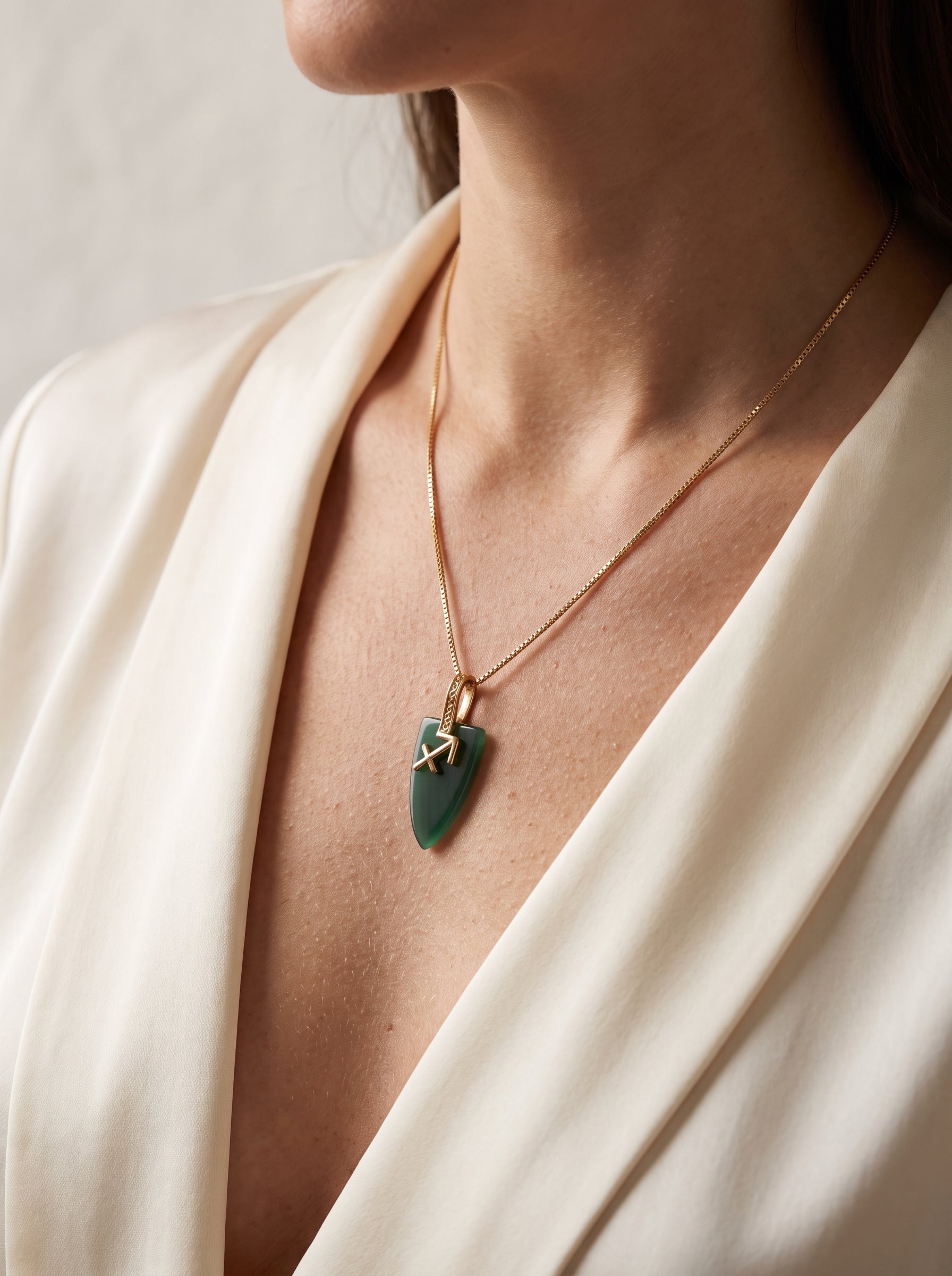 Close-up of green agate Sagittarius zodiac pendant necklace on a gold box chain worn against bare skin