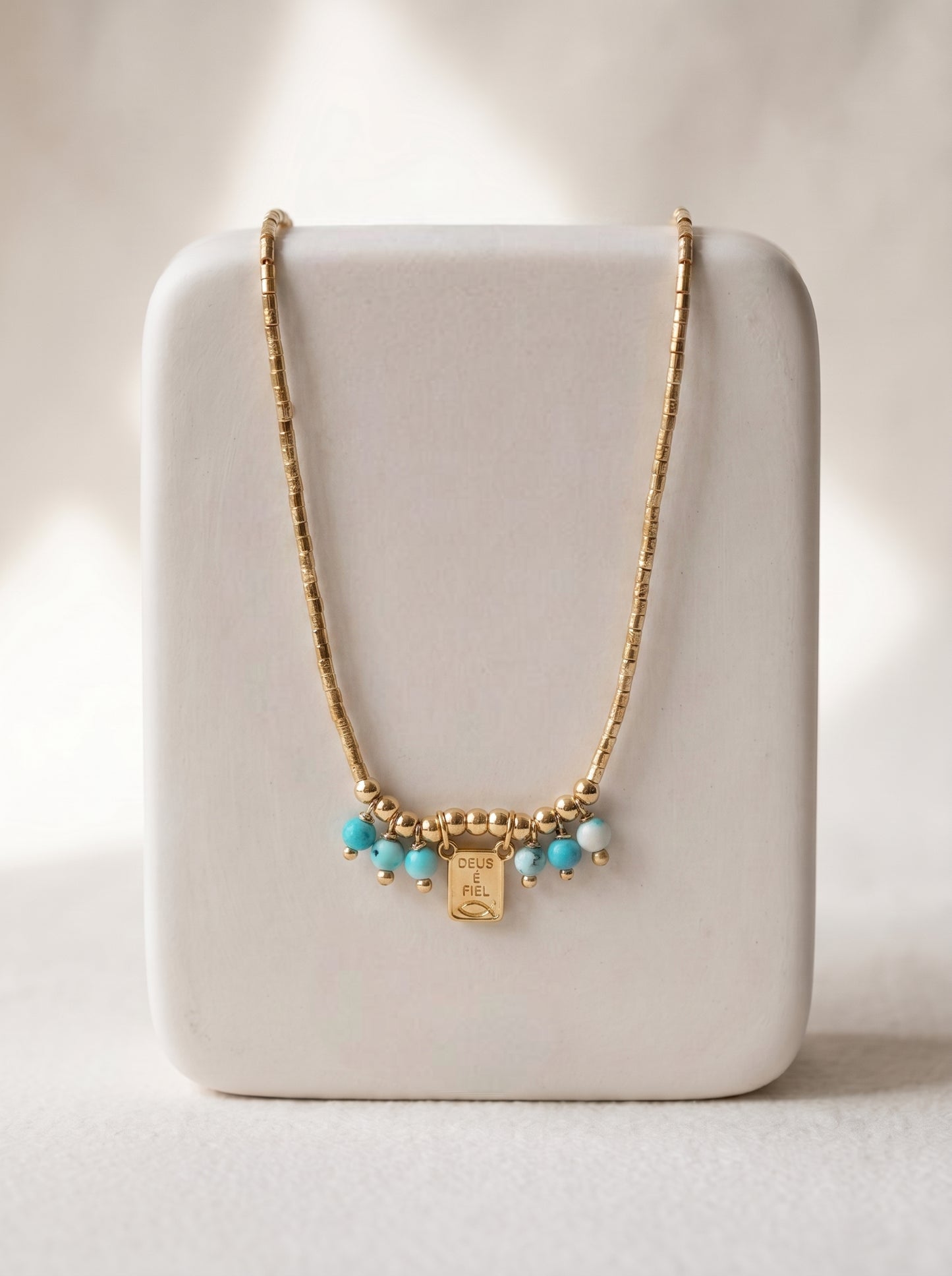  Gold tube bead necklace with natural turquoise beads and engraved square charm displayed on a white jewellery stand