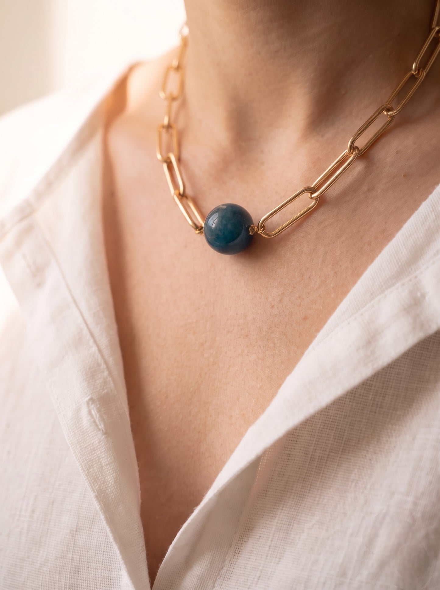 Woman wearing StoneCraft Jewellery apatite gemstone sphere gold paperclip chain necklace, white linen shirt close-up.