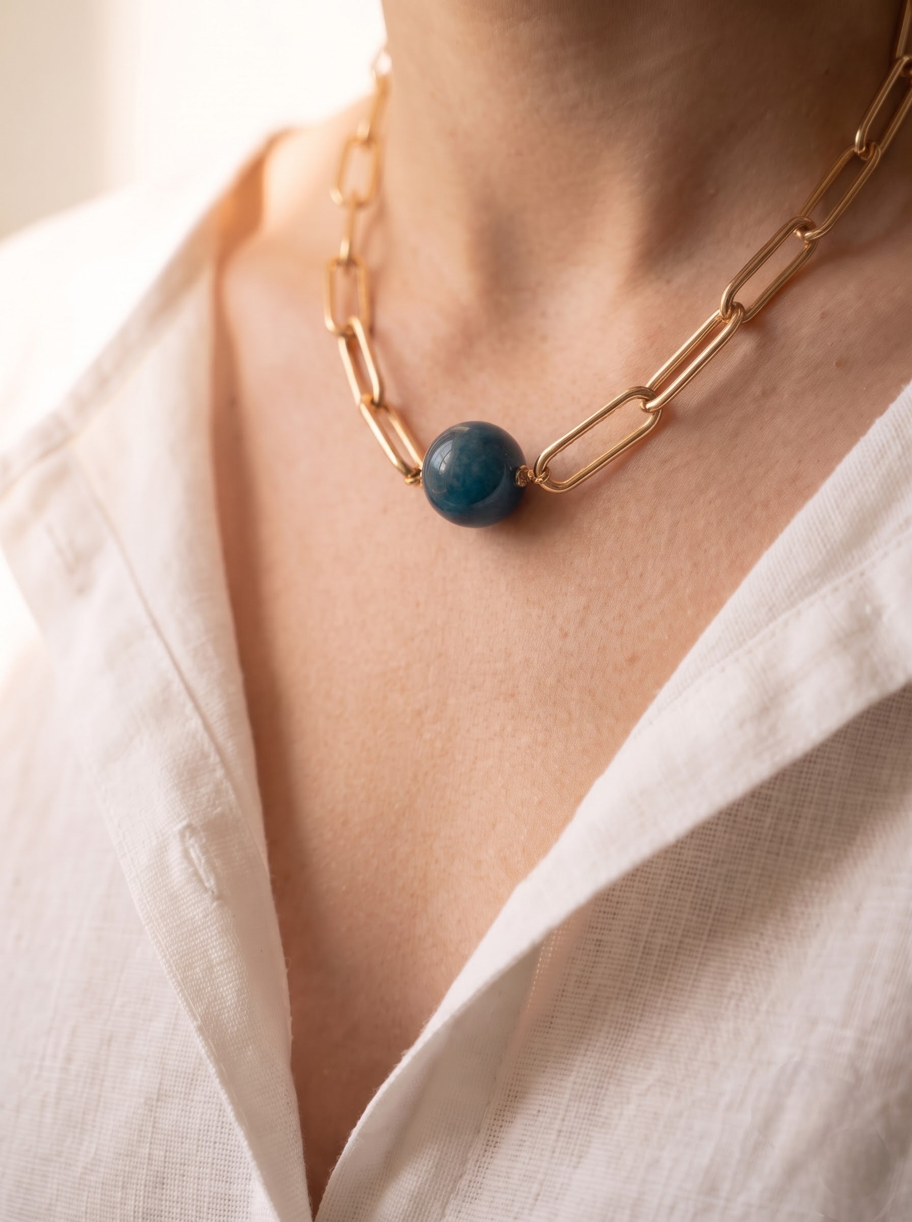 Woman wearing StoneCraft Jewellery apatite gemstone sphere gold paperclip chain necklace, white linen shirt close-up.