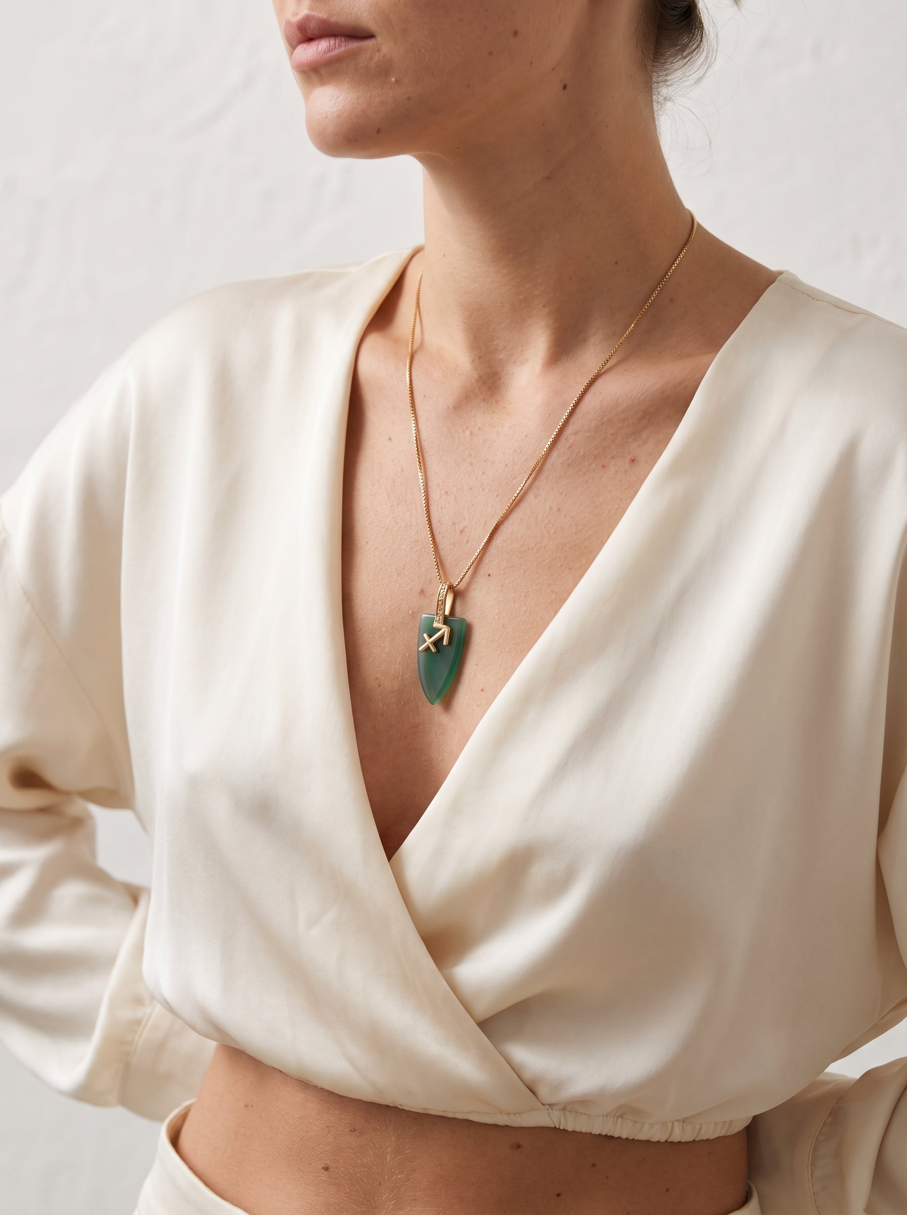 Sagittarius agate pendant necklace with gold zodiac symbol worn by a woman in a cream wrap top