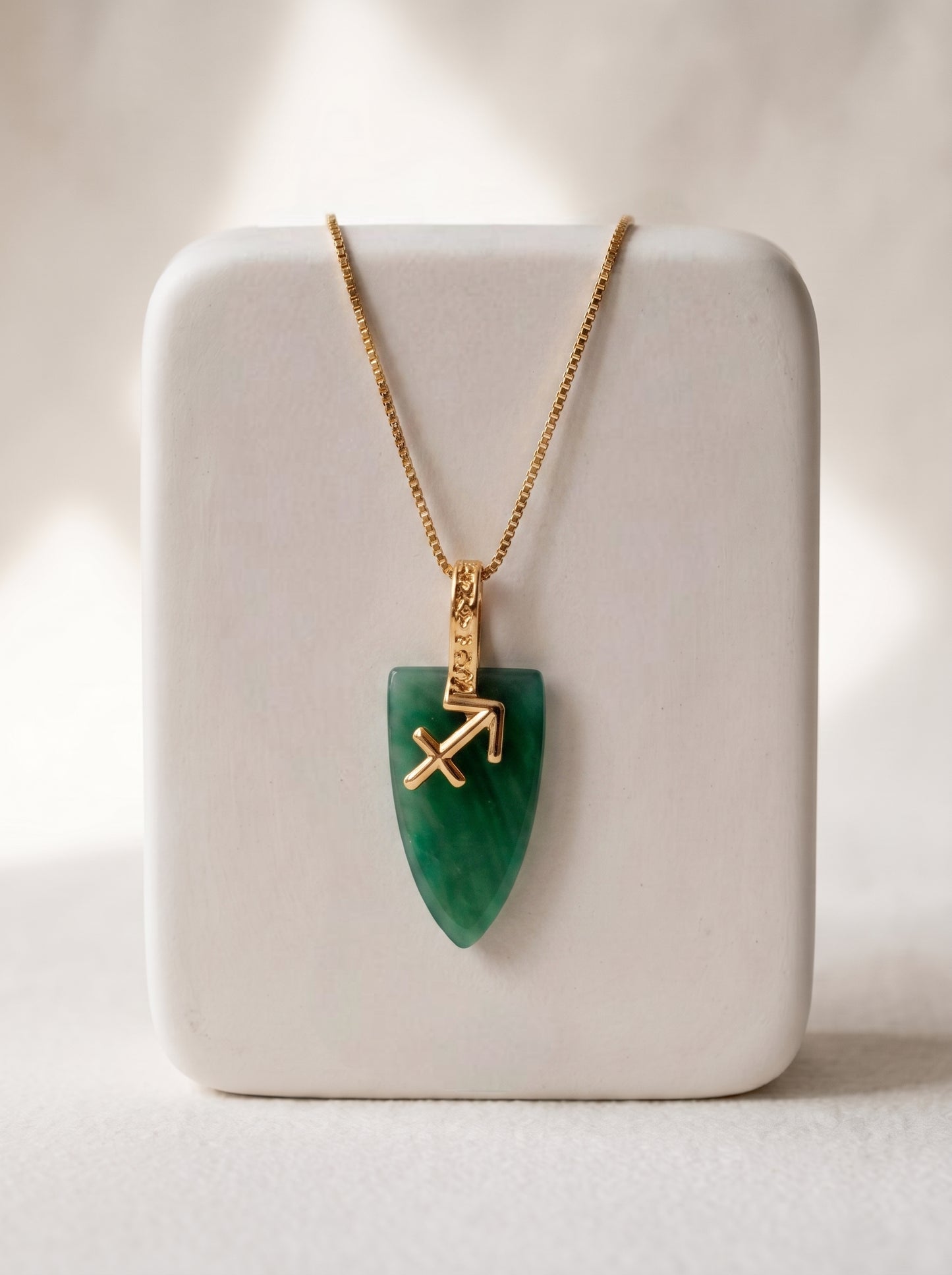 Gold-plated box chain necklace with green agate arrowhead pendant and Sagittarius zodiac symbol displayed on a white jewellery stand