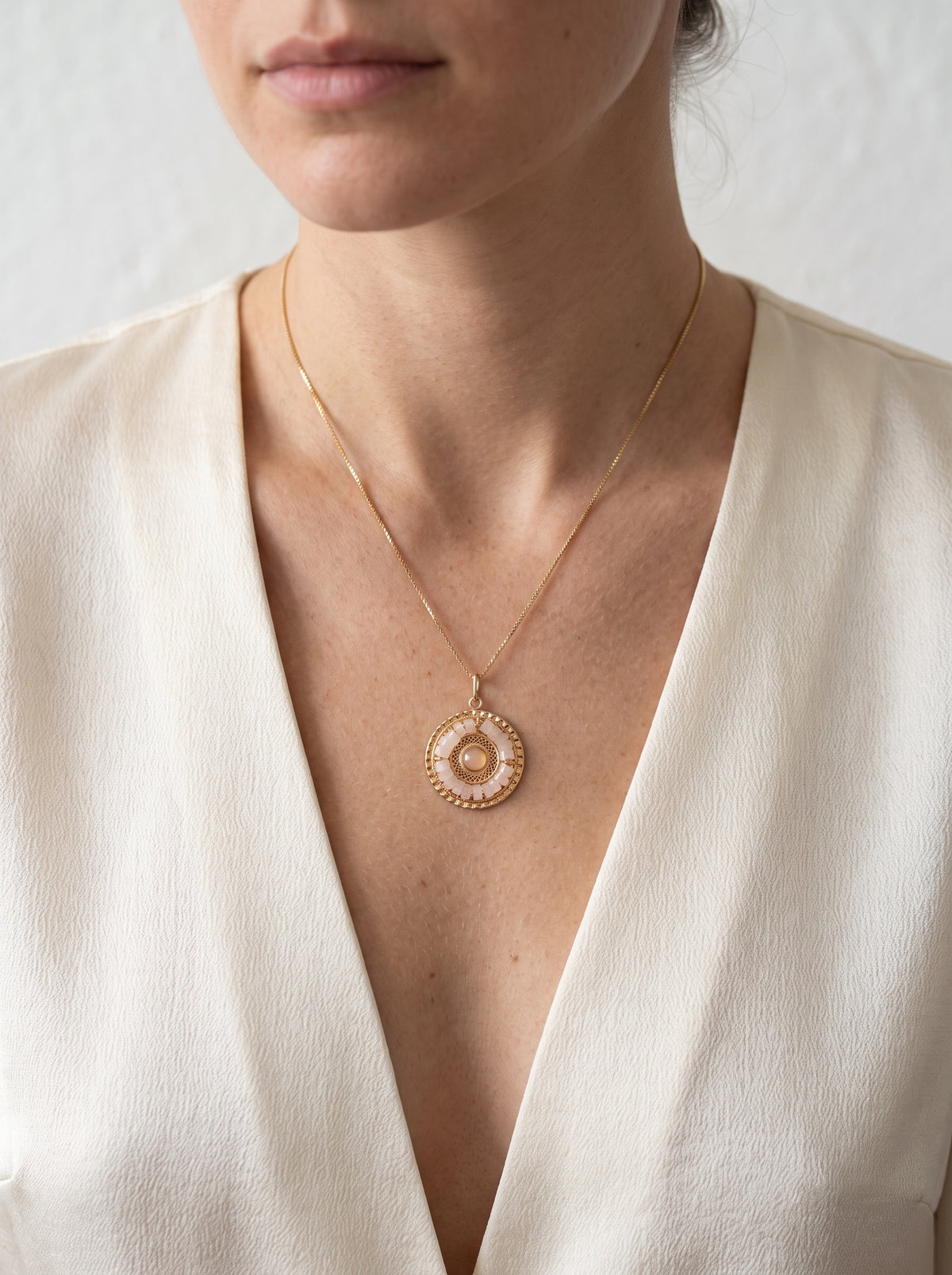 A close-up of a model wearing a delicate gold chain necklace with a  manadala rose quartz circular pendant.