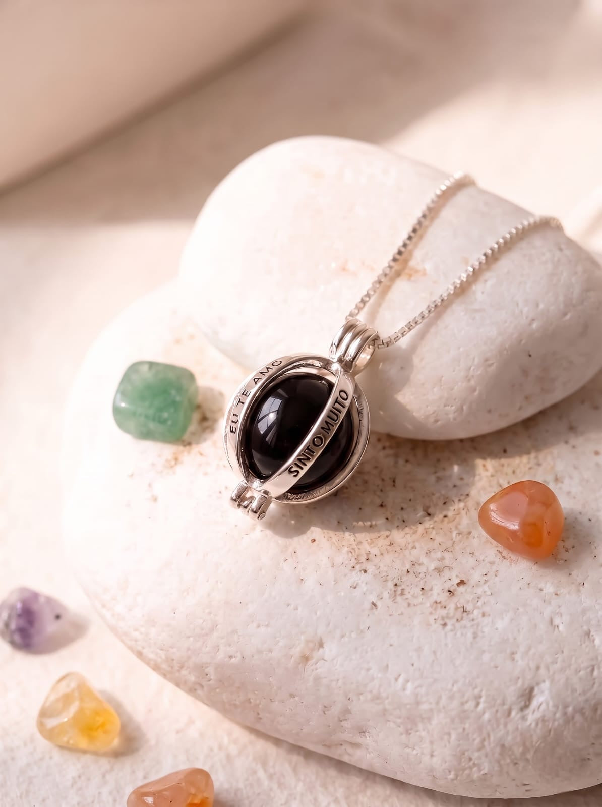StoneCraft Jewellery Angel Caller Necklace Rhodium Plated with Black Agate displayed on white pebble stones with colourful gemstones