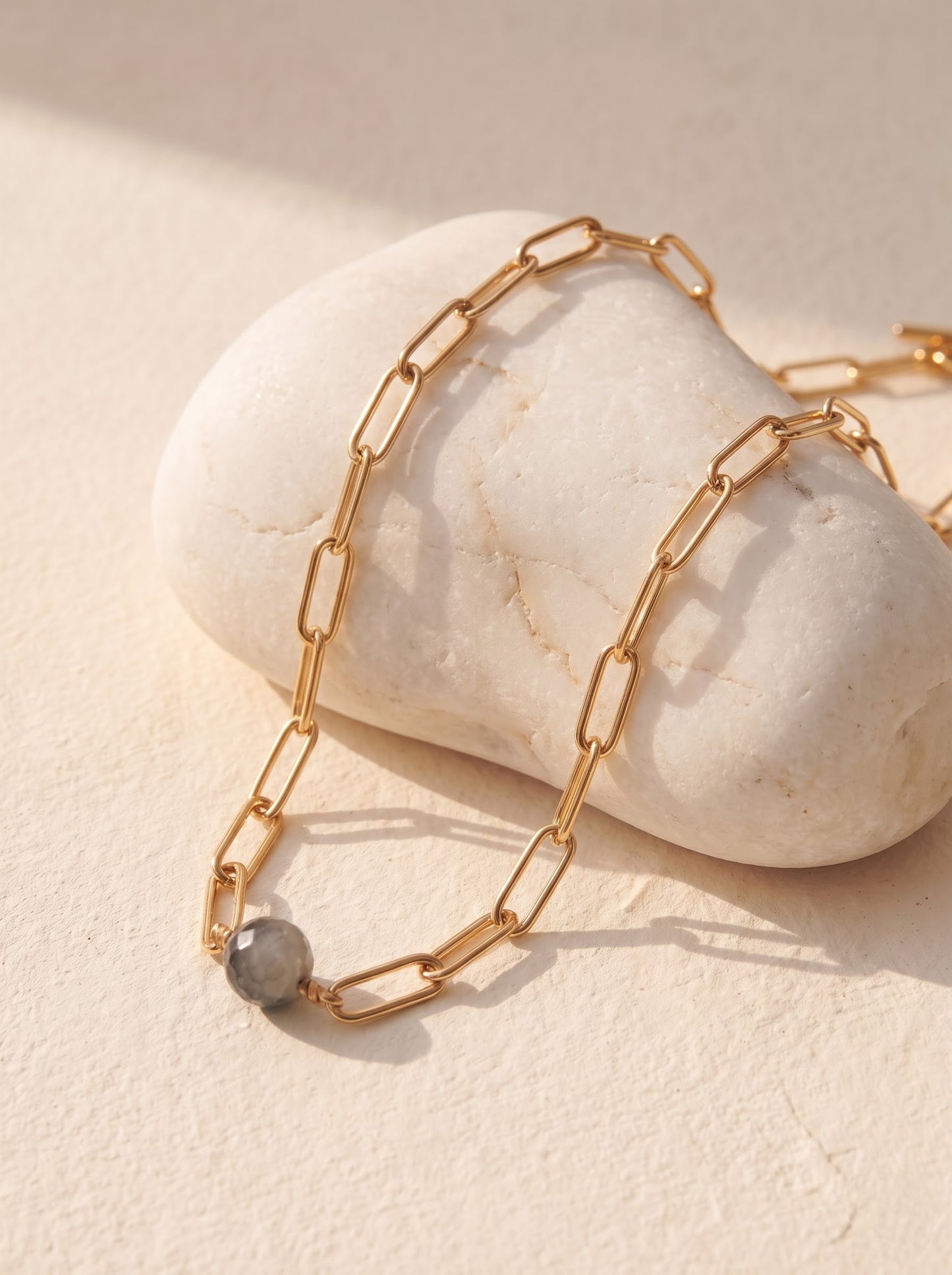 StoneCraft Jewellery black rutile quartz sphere gold paperclip chain necklace, flat lay on white stone surface.