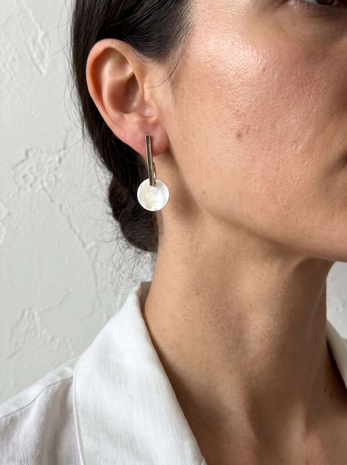Model wearing gold bar drop earrings with mother of pearl disc, close-up side profile