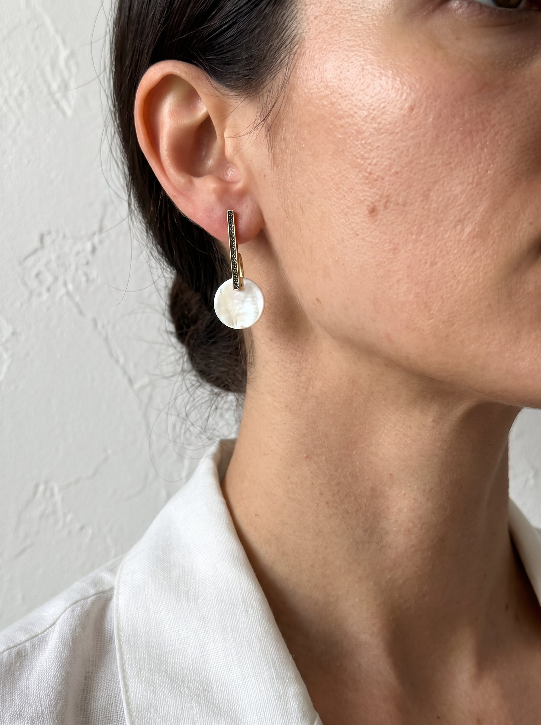 Model wearing gold bar drop earrings with mother of pearl disc, close-up side profile