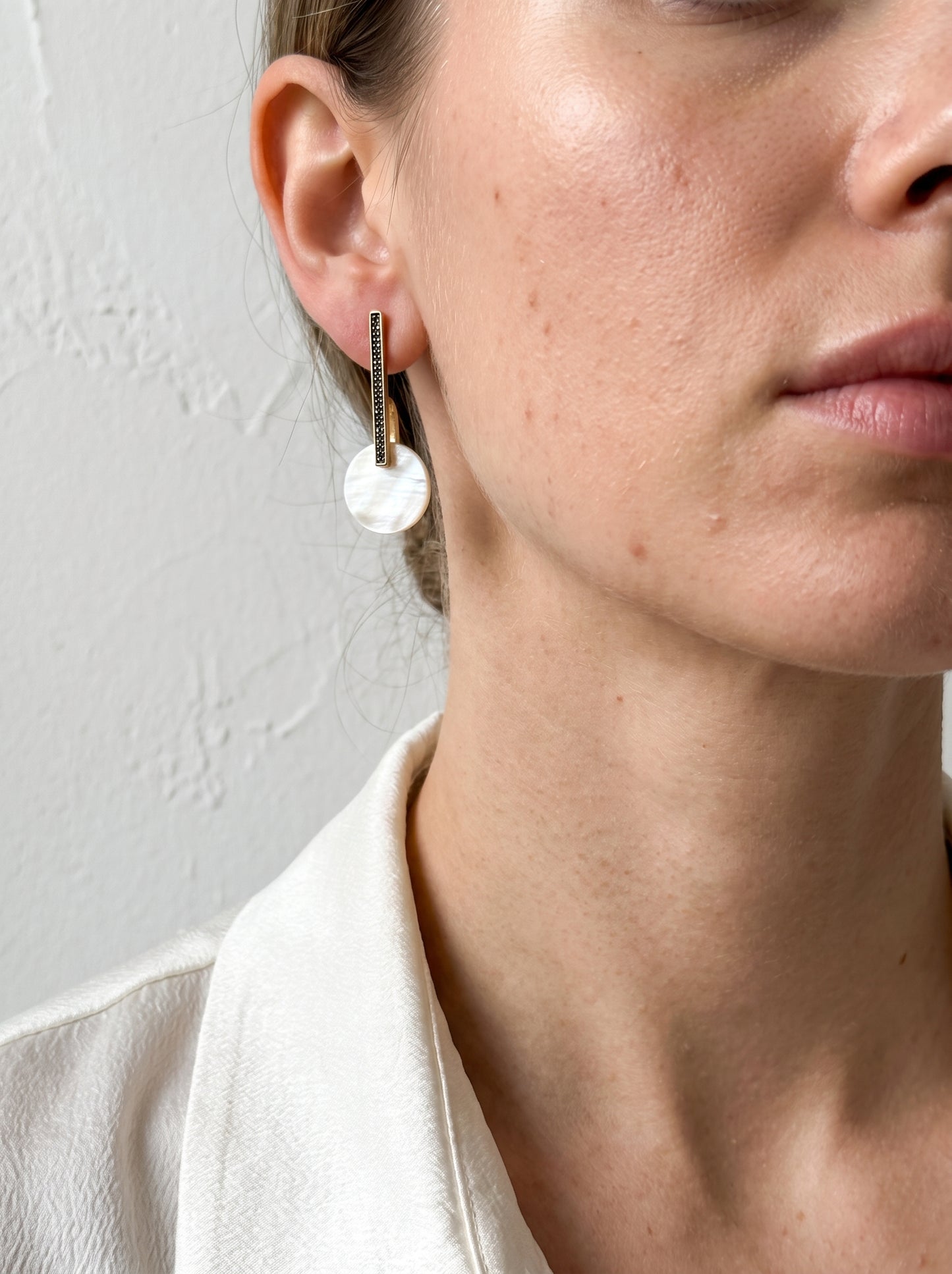 Model wearing mother of pearl bar drop earrings in gold with black pavé crystals, side view