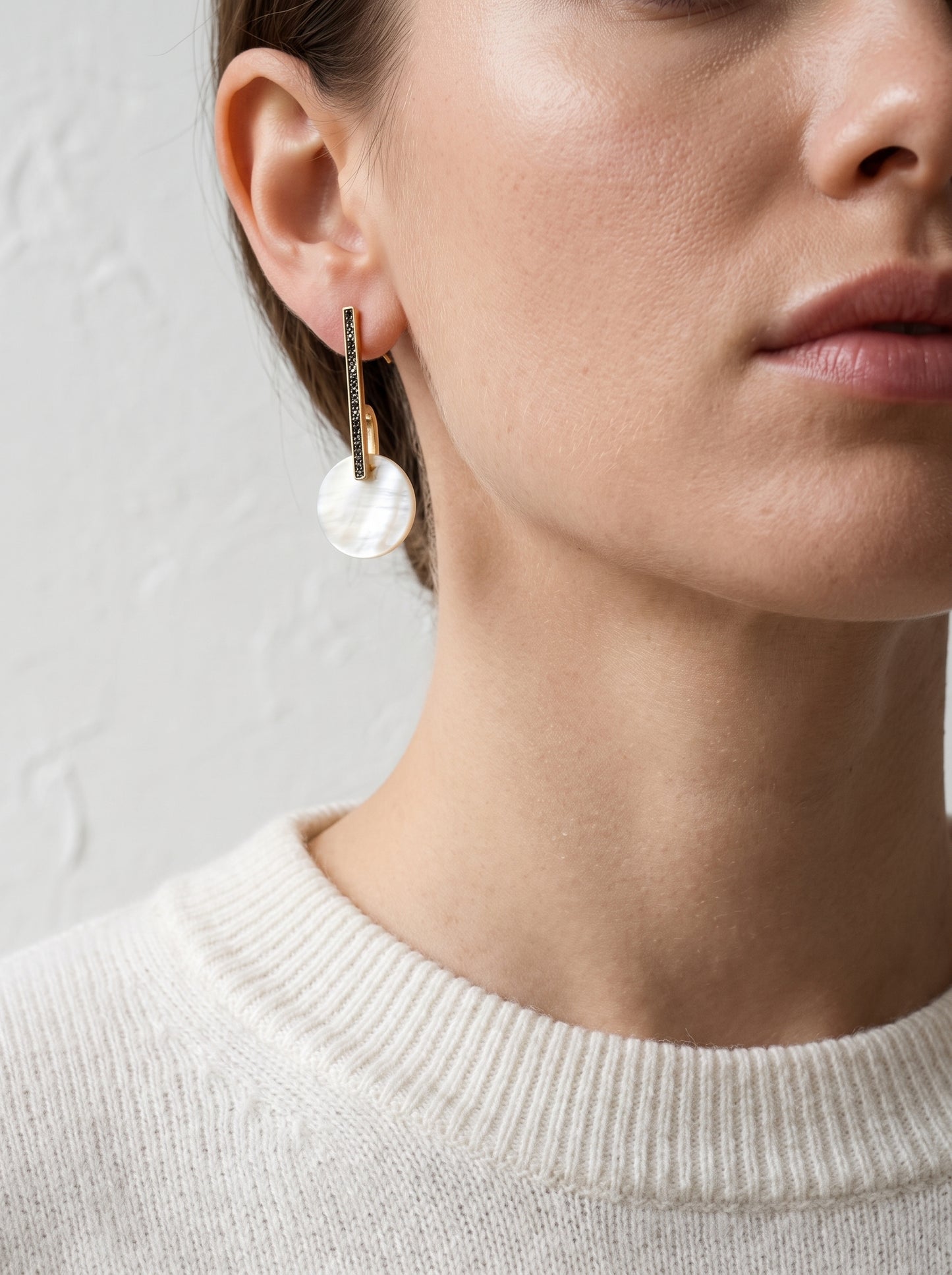 Model wearing gold and mother of pearl bar drop earrings with cream knit jumper